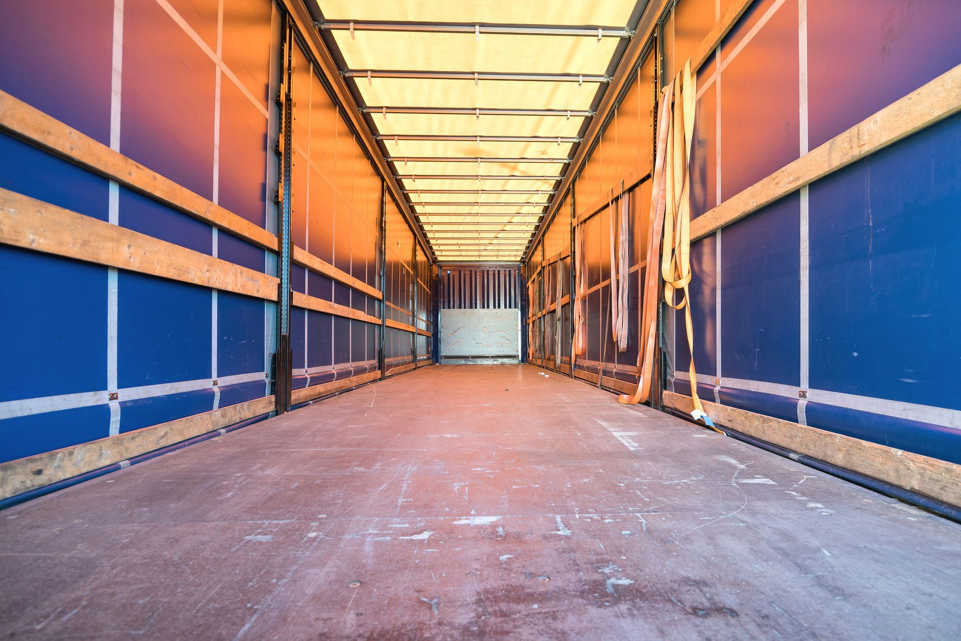 Empty semi-truck trailer interior with blue side walls, wooden supports, and a light-colored floor.