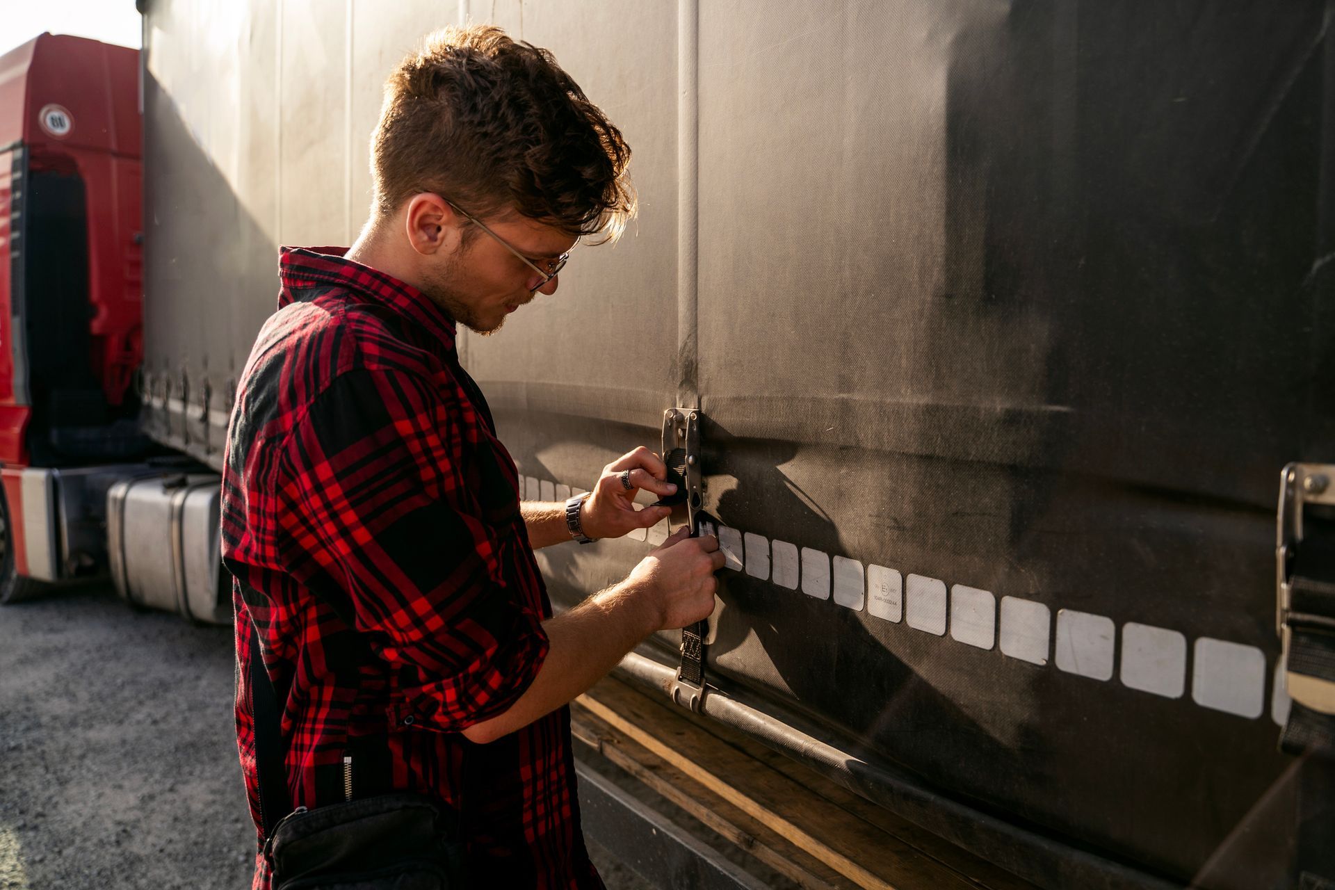 Man in red plaid shirt unlocks a truck's side door in daylight.