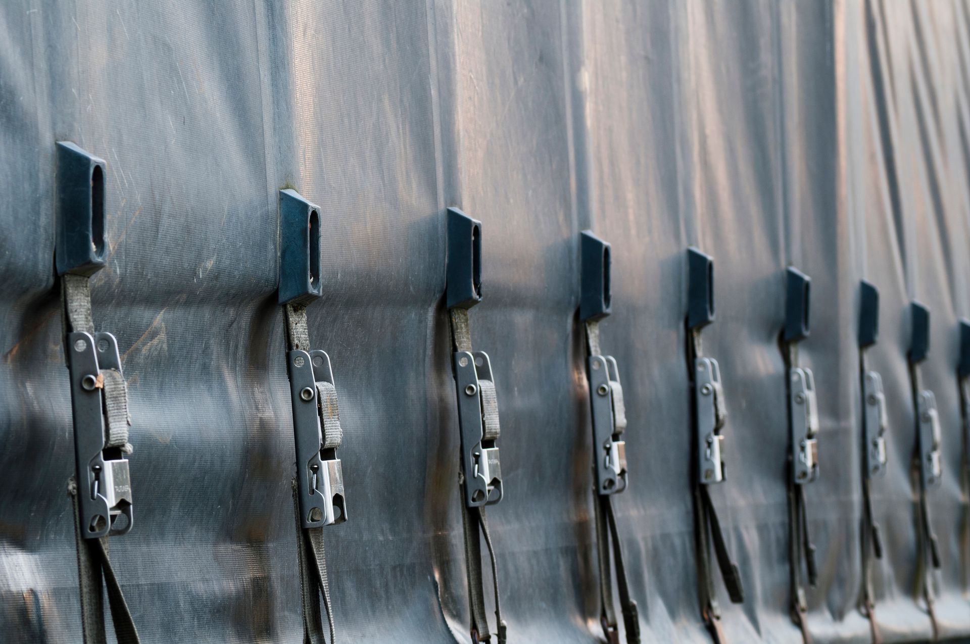 Close-up of a row of metal latches securing a black tarp on a truck trailer.