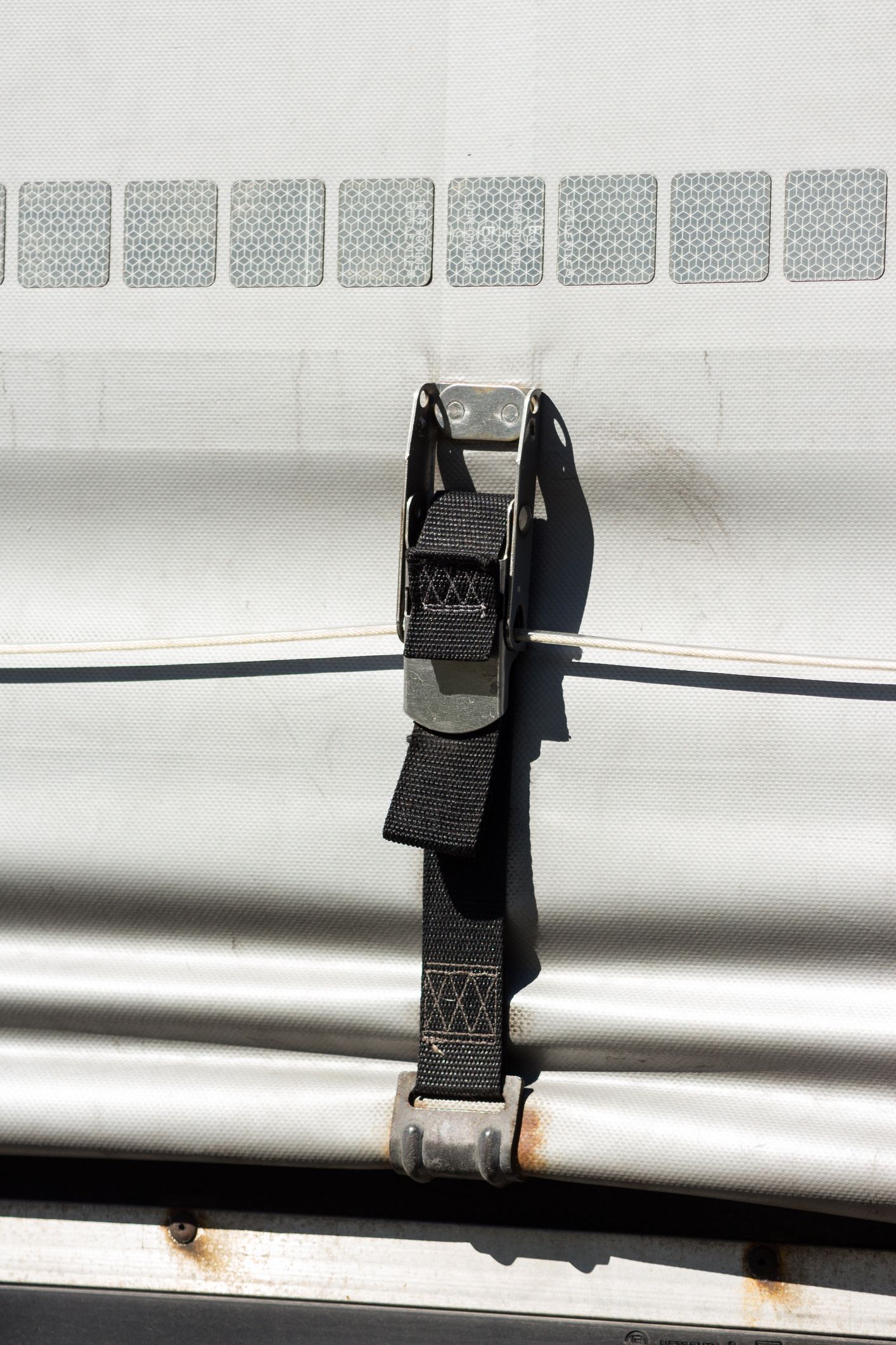 Black strap securing a white tarp with a metal buckle and rusted metal bracket.