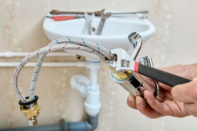 Plumber using wrench to connect water line to faucet in a bathroom.