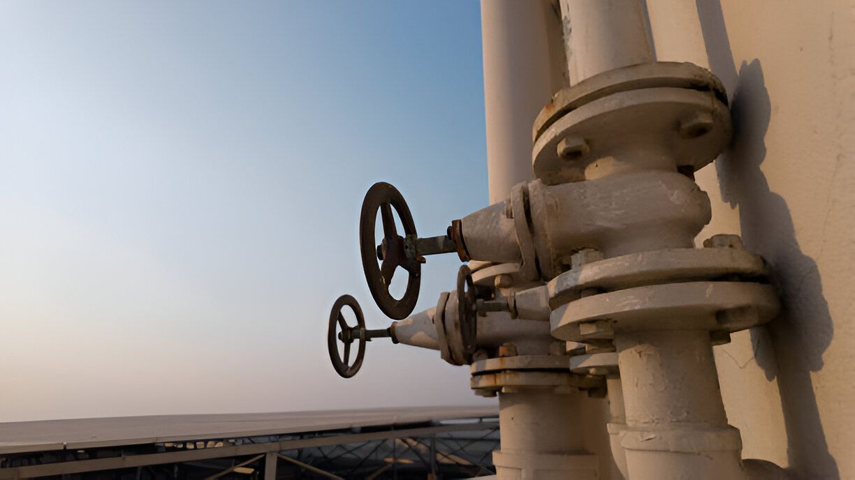 A close up of a valve on a pipe with a blue sky in the background.