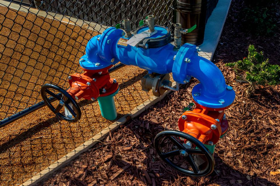 A blue pipe with two red valves attached to it is sitting next to a chain link fence.