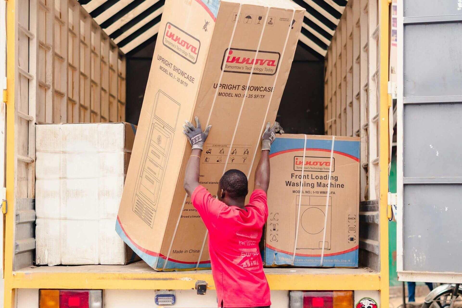 men in red shirt placing box of fridge appliance next to other appliance boxes in truck
