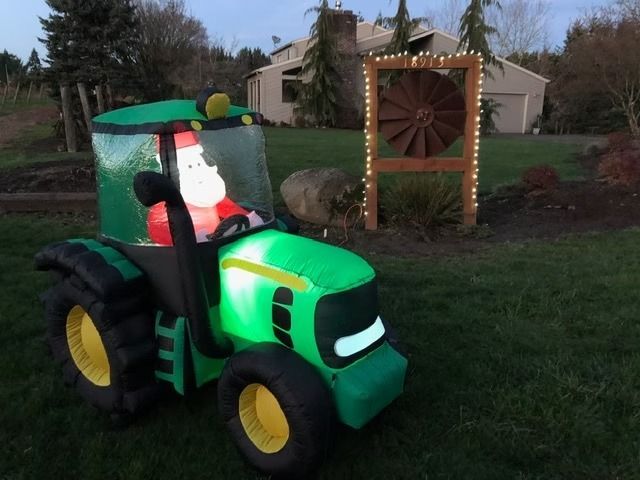 Green toy tractor with a Santa figure, parked on grass beside a wooden windmill decoration.