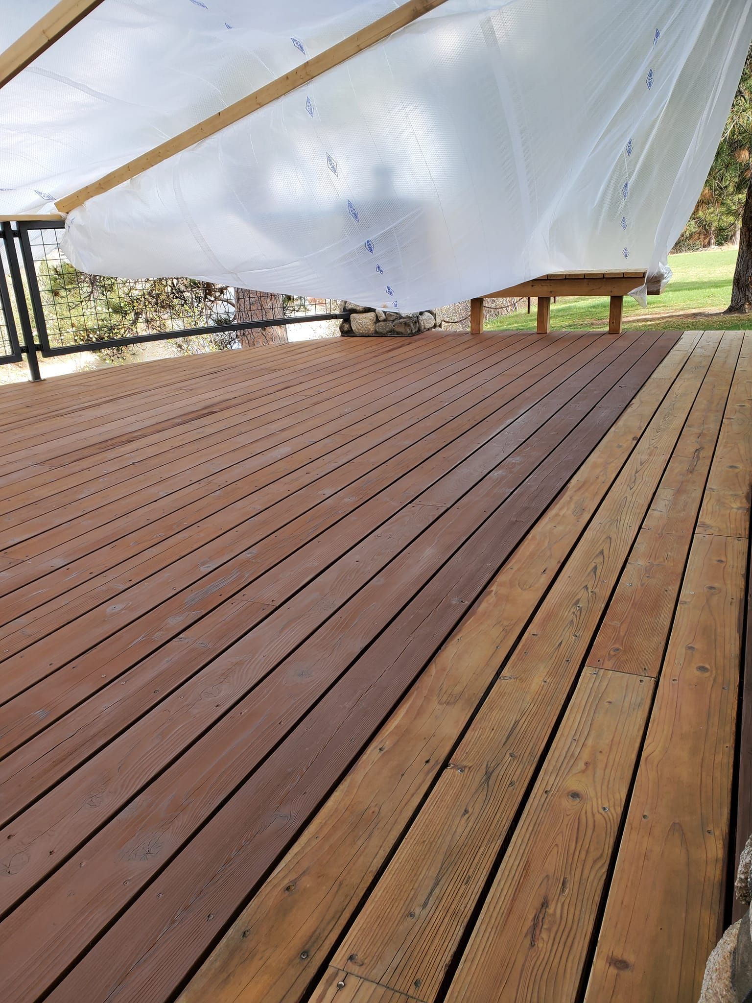 Wooden deck with brown and light wood planks, covered by a white tarp, under a wooden structure.