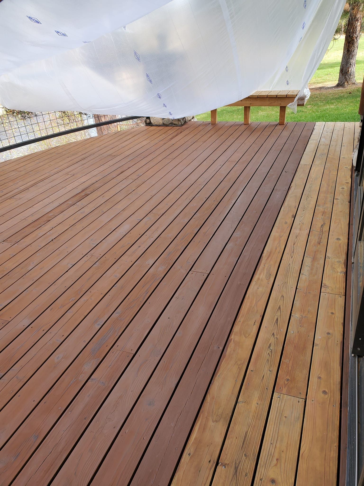 Wooden deck with light-colored, aged boards on the right. Shaded by a white canopy, with a bench visible.