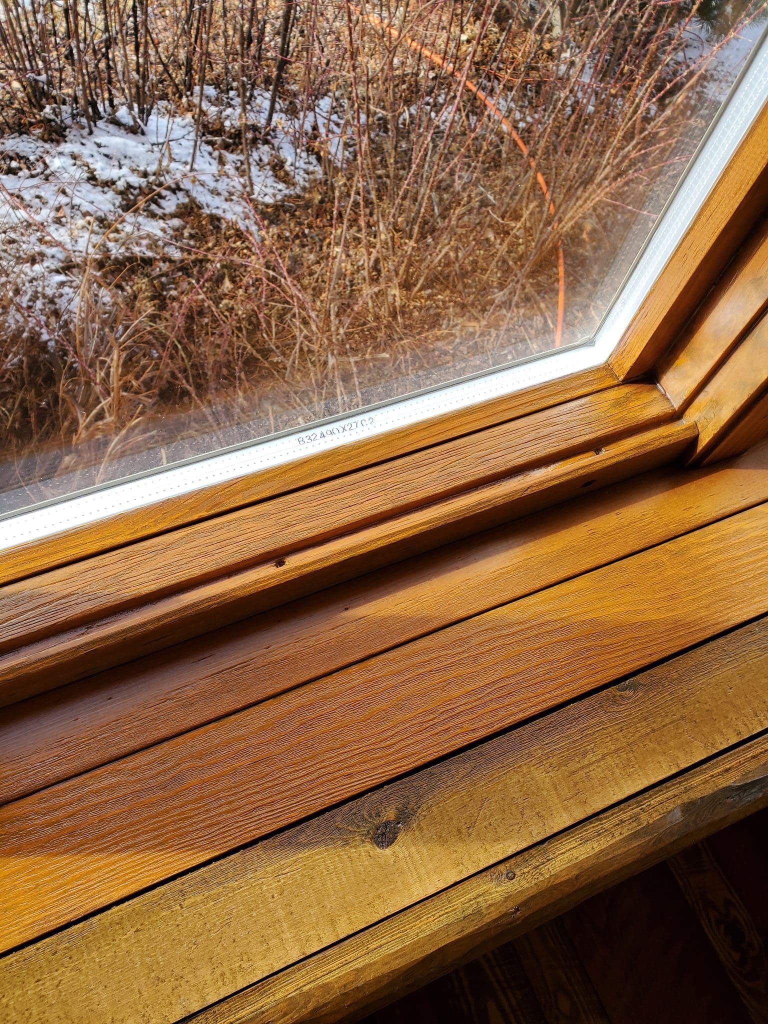 Wooden window frame with condensation; view of snow and branches outside.