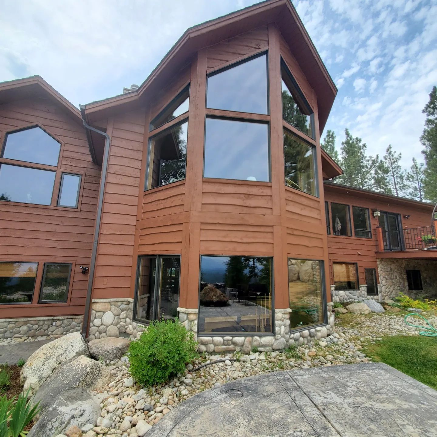 Brown house with large windows, surrounded by rocks and a grassy lawn, under a cloudy sky.