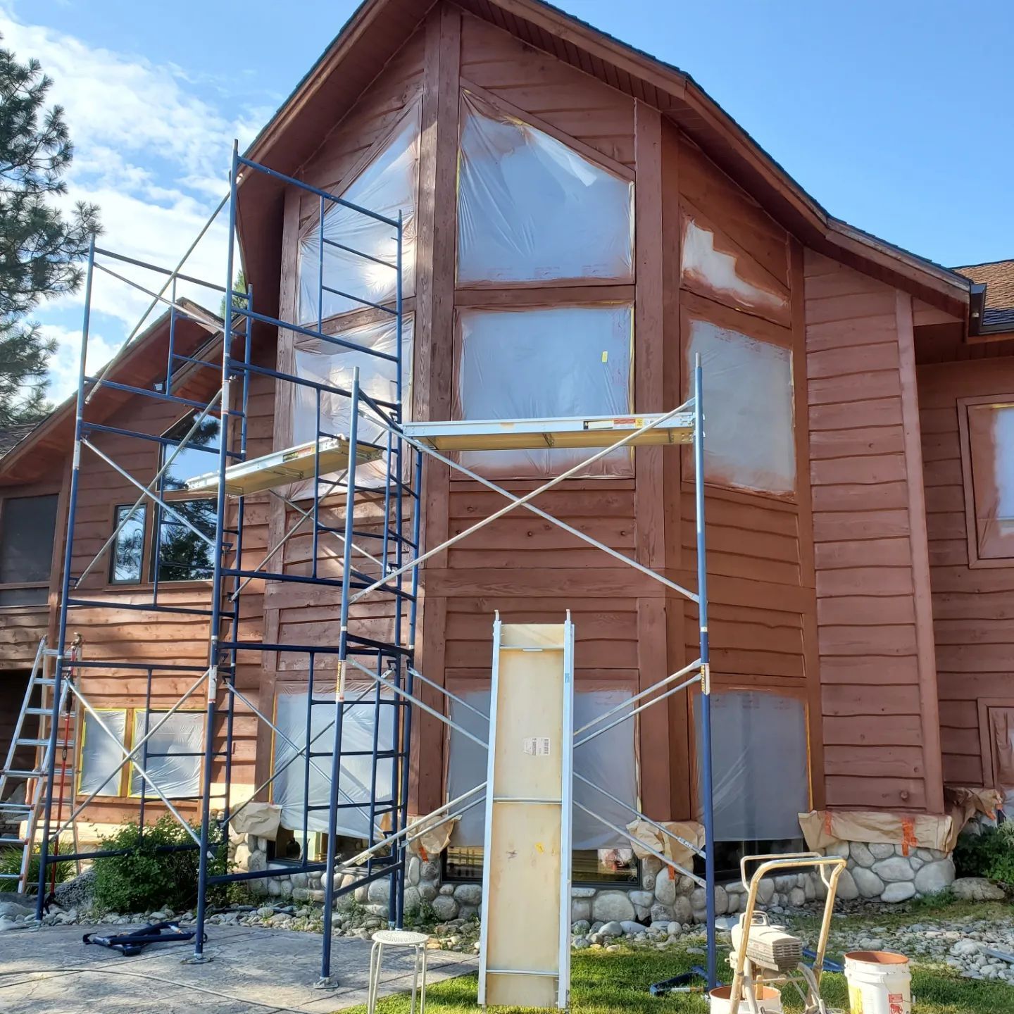 House exterior being painted, with scaffolding and plastic covering windows.