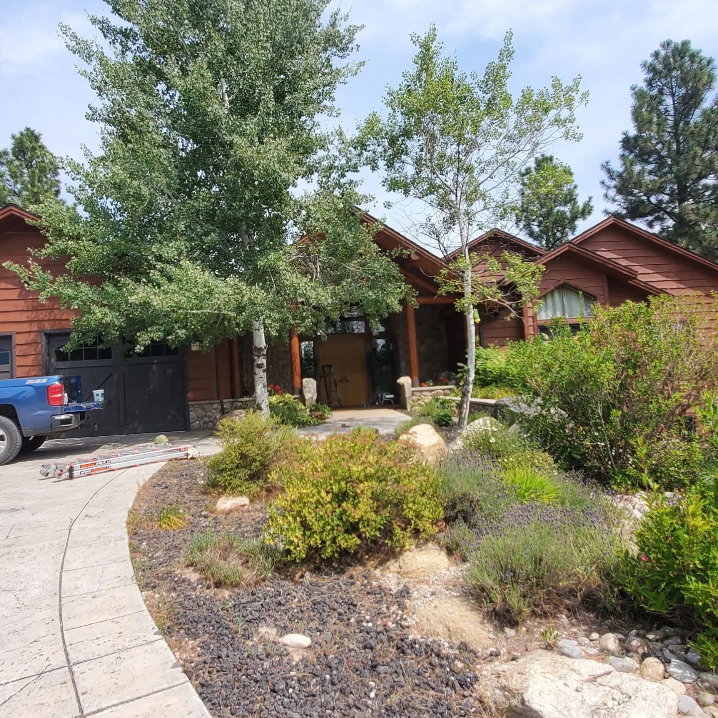Brown cabin-style home with landscaping, driveway, and a blue truck parked beside a garage door.