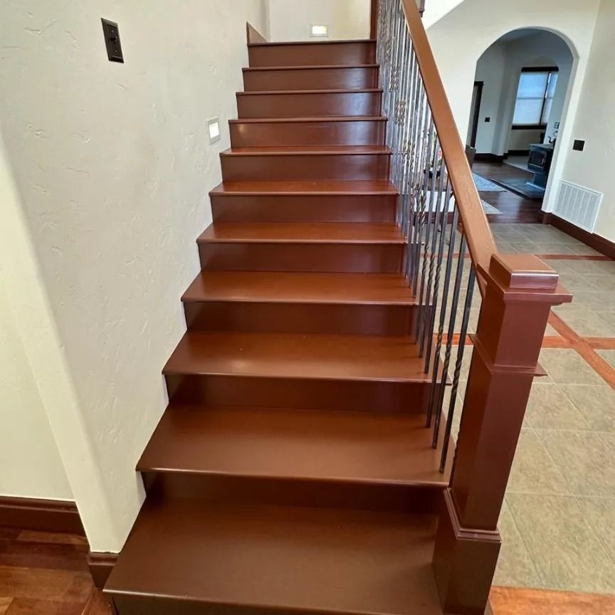 Staircase with brown wooden steps, railing, and newel post. Entryway with tile and hardwood flooring.