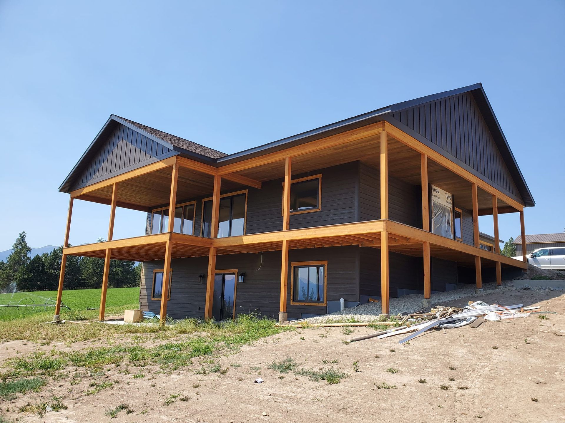 Two-story house with dark siding and a brown deck, under construction on a sunny day.