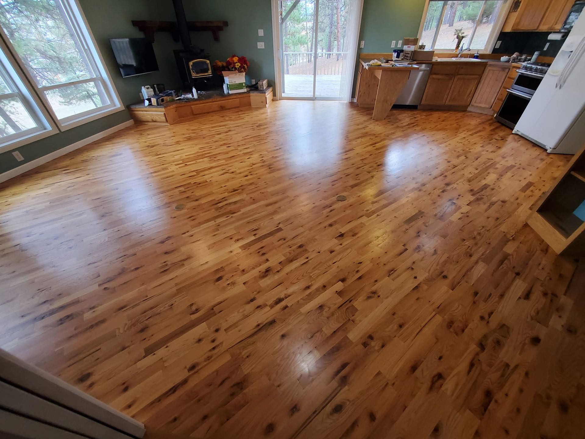 Wooden floor in a bright room with windows, kitchen cabinets, and a fireplace.