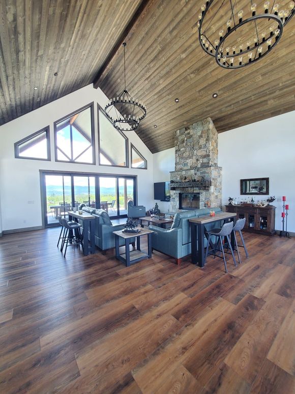 Spacious living room with wood floors, vaulted wood ceiling, stone fireplace, and large windows.