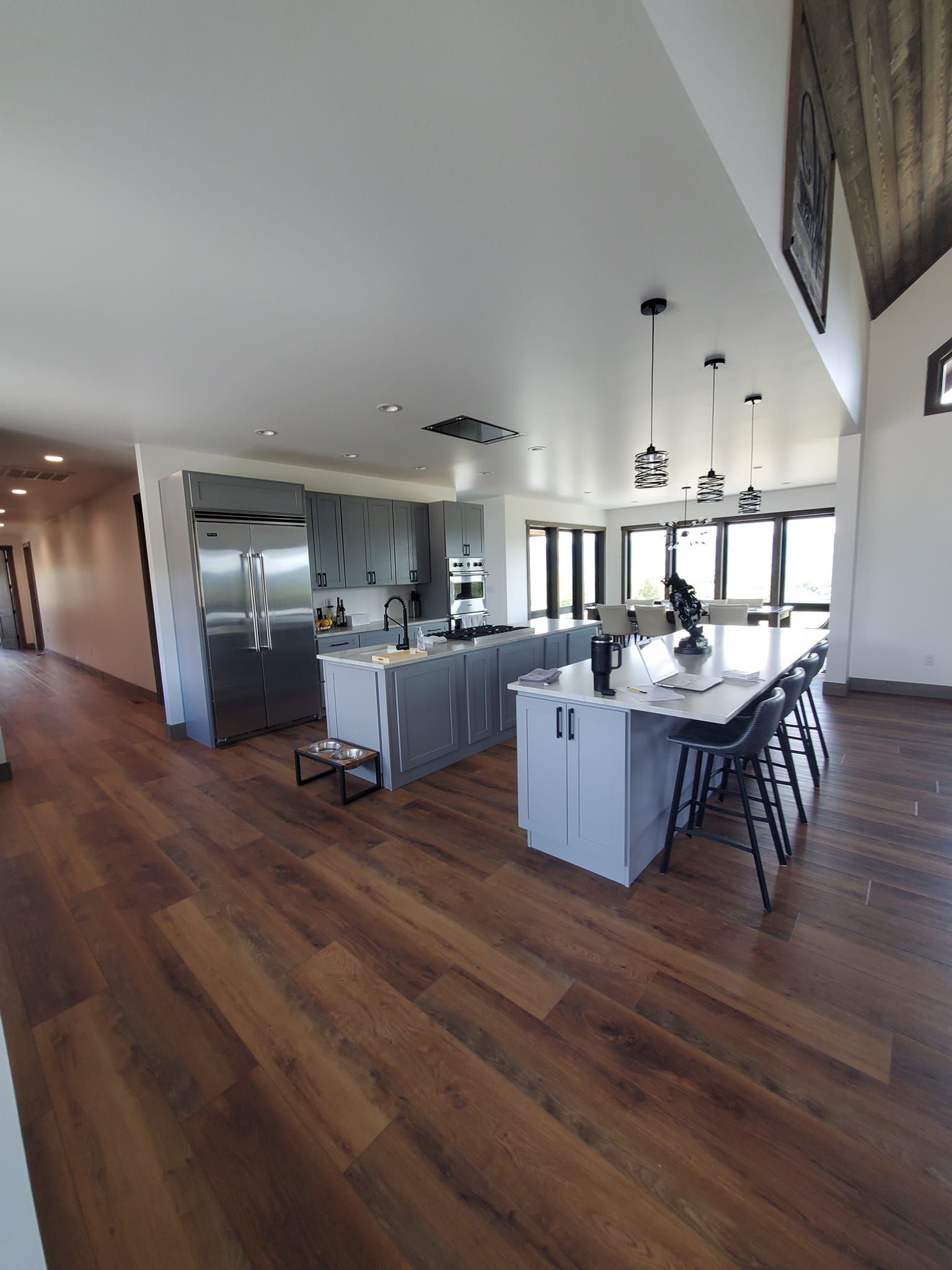 Spacious kitchen with gray cabinets, large island, stainless steel fridge, and wood floors.