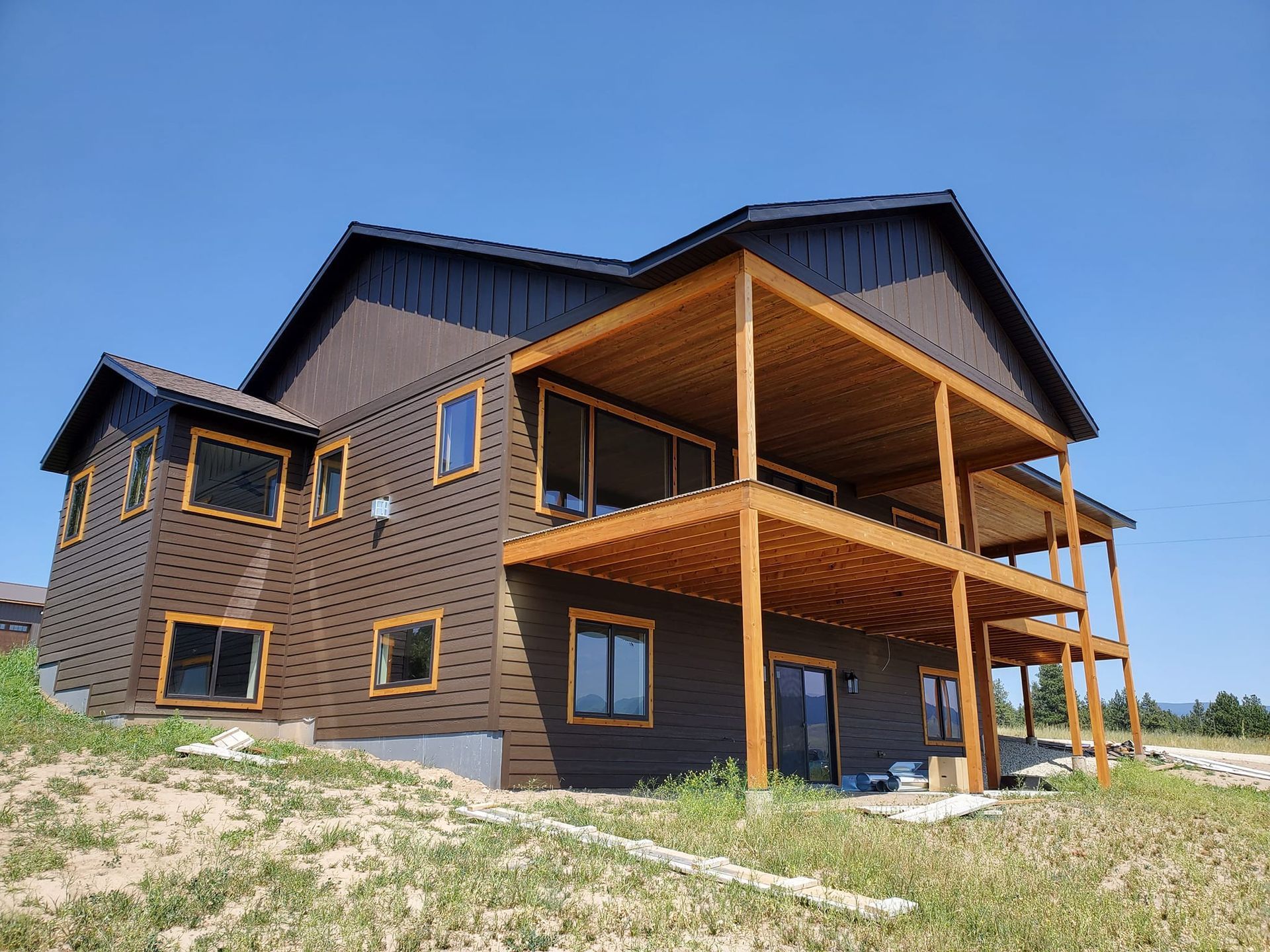 Two-story brown house with a wooden deck and tan trim on a sunny day.