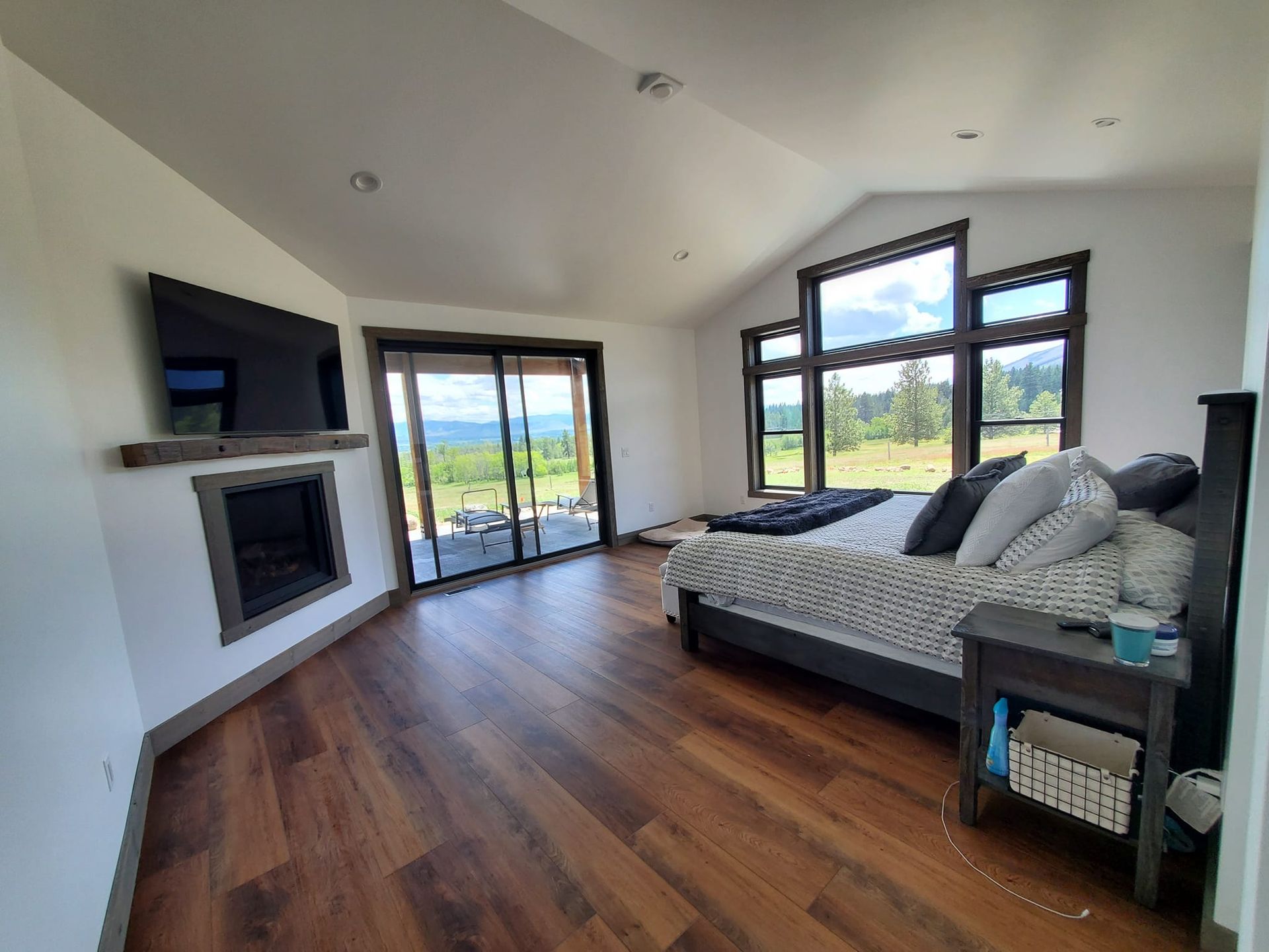 Bedroom with fireplace, bed, and large windows overlooking a scenic landscape. Hardwood floors and dark trim.
