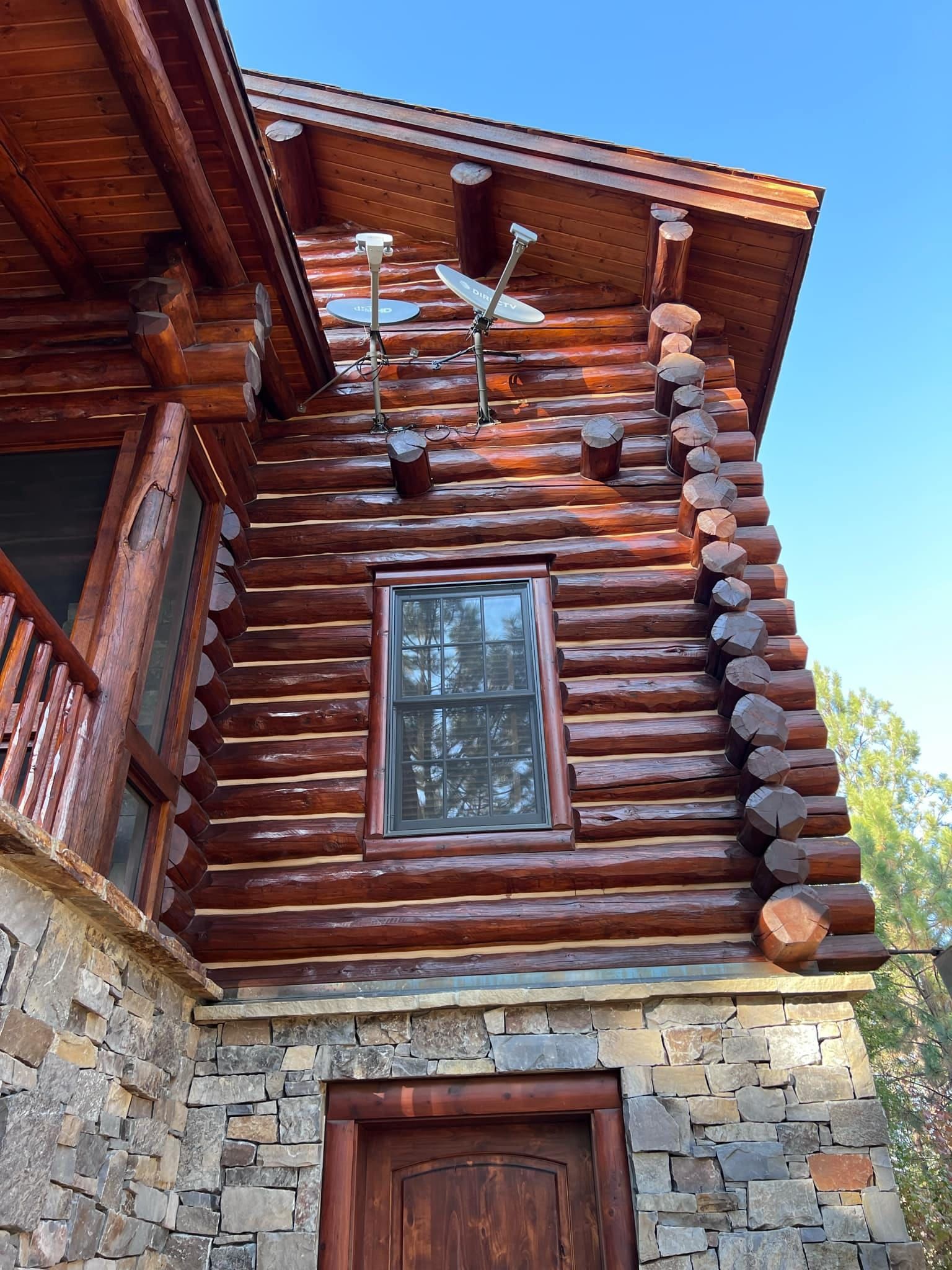 Log cabin with stone foundation and brown wooden door and window, satellite dishes.