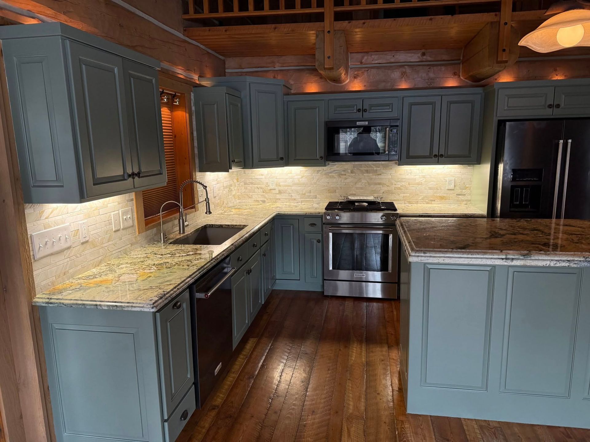 Kitchen with blue-gray cabinets, stainless steel appliances, granite countertops, and wood floors.