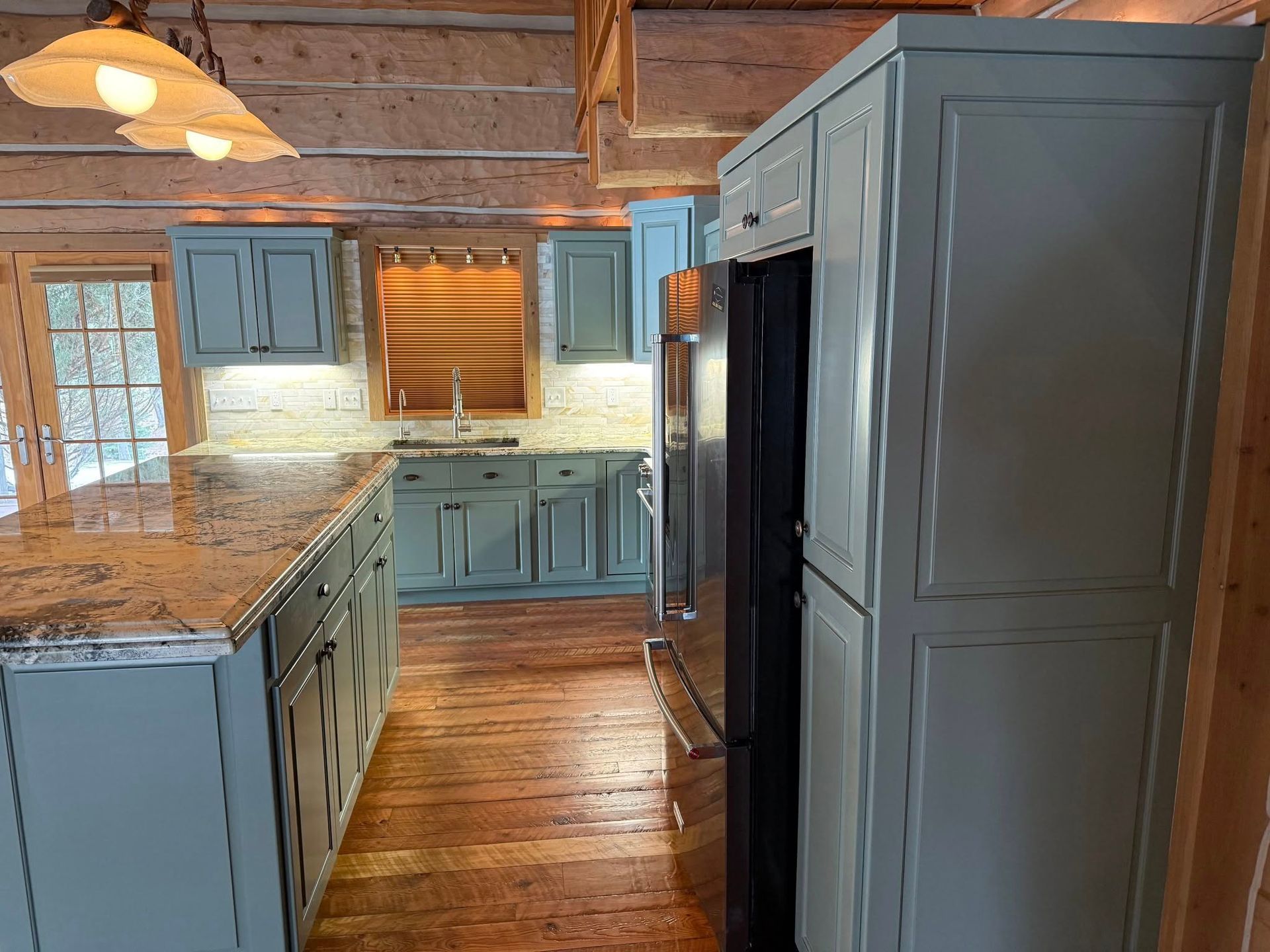 Kitchen with blue cabinets, granite countertops, and stainless steel refrigerator in a log cabin.