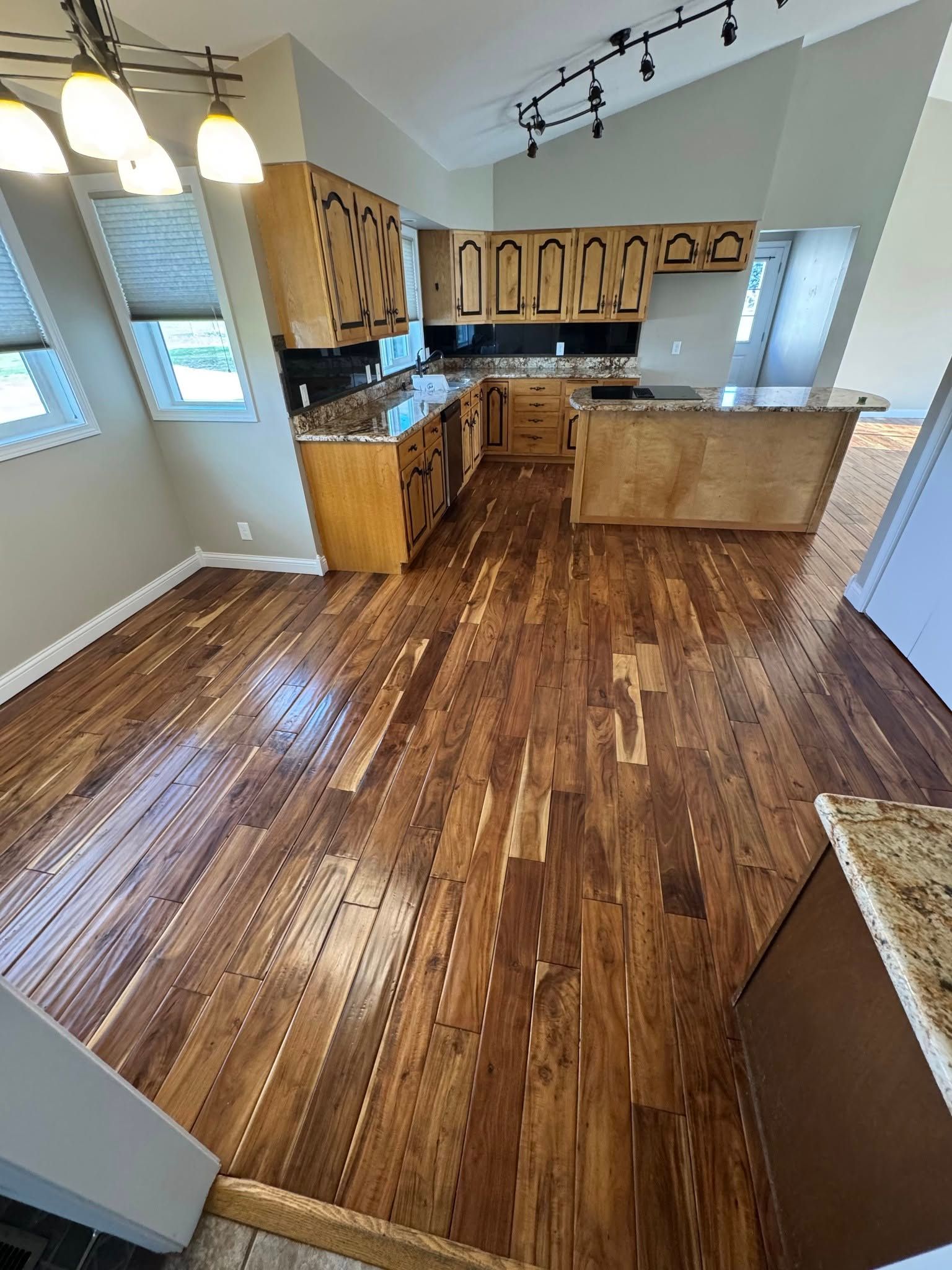 Hardwood floors in a kitchen with wooden cabinets and a granite countertop, bathed in natural light.
