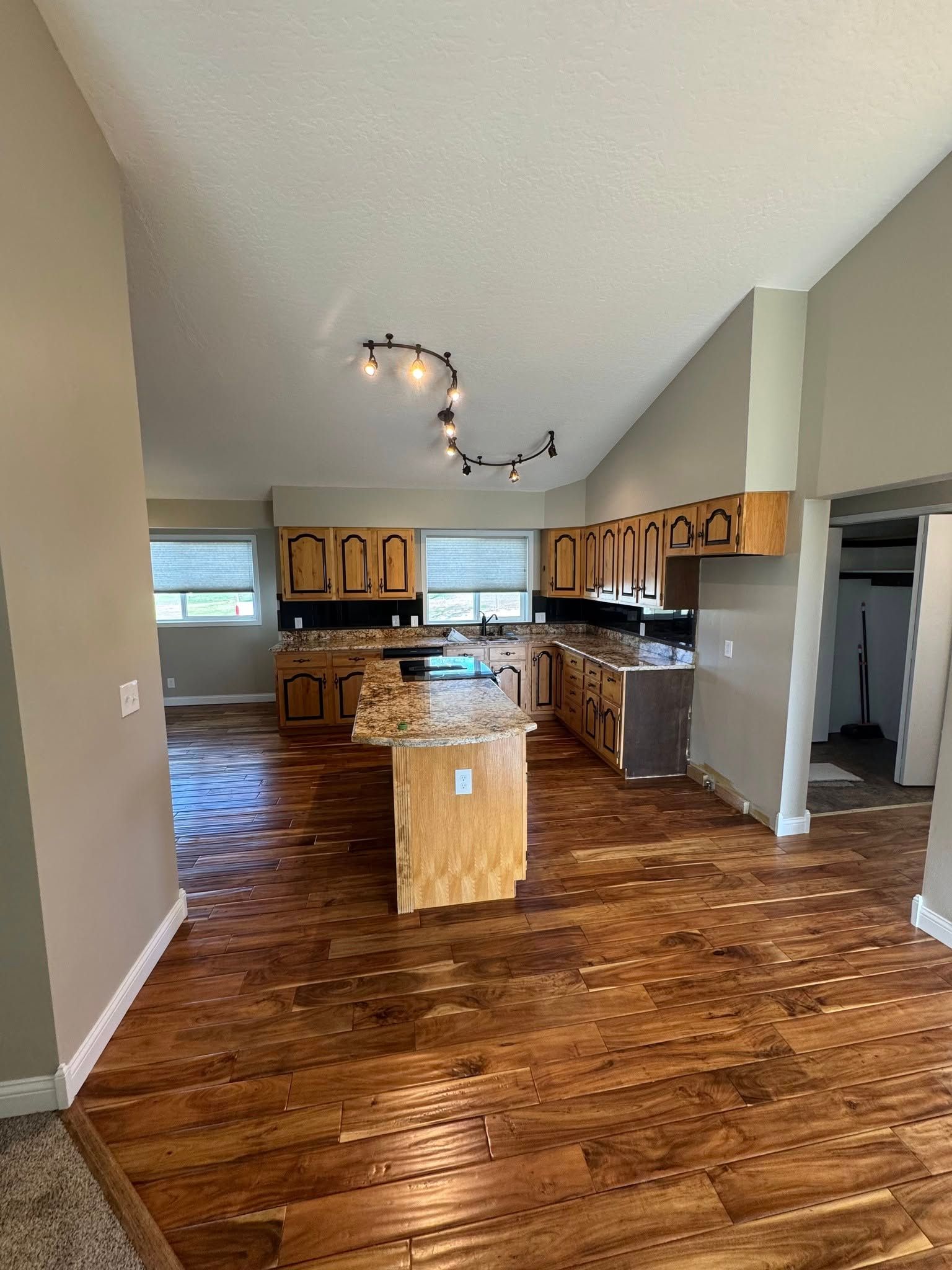 Kitchen with wood cabinets, island, and flooring. Light-colored walls and track lighting.