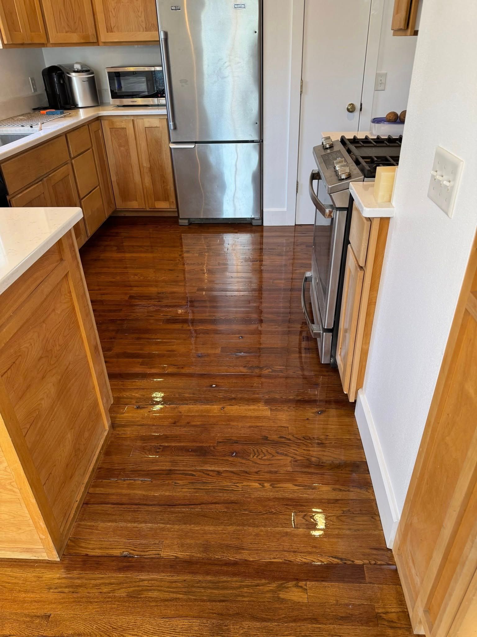 Wooden kitchen floor with dark brown stain. Cabinets, refrigerator, and stove are visible.