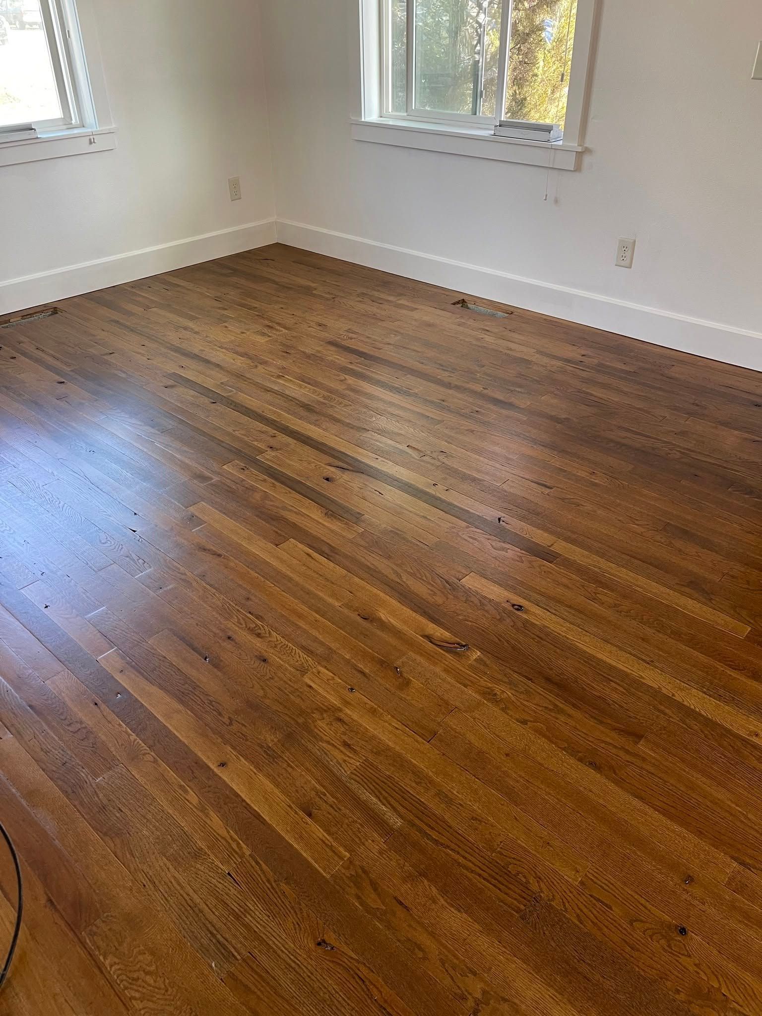 Hardwood floors in a room, two windows on the wall. The floors are various shades of brown.
