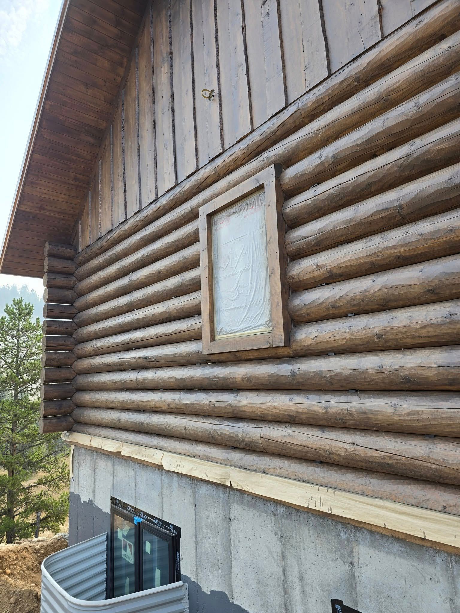 Log cabin exterior with brown logs, a window, and a concrete foundation.