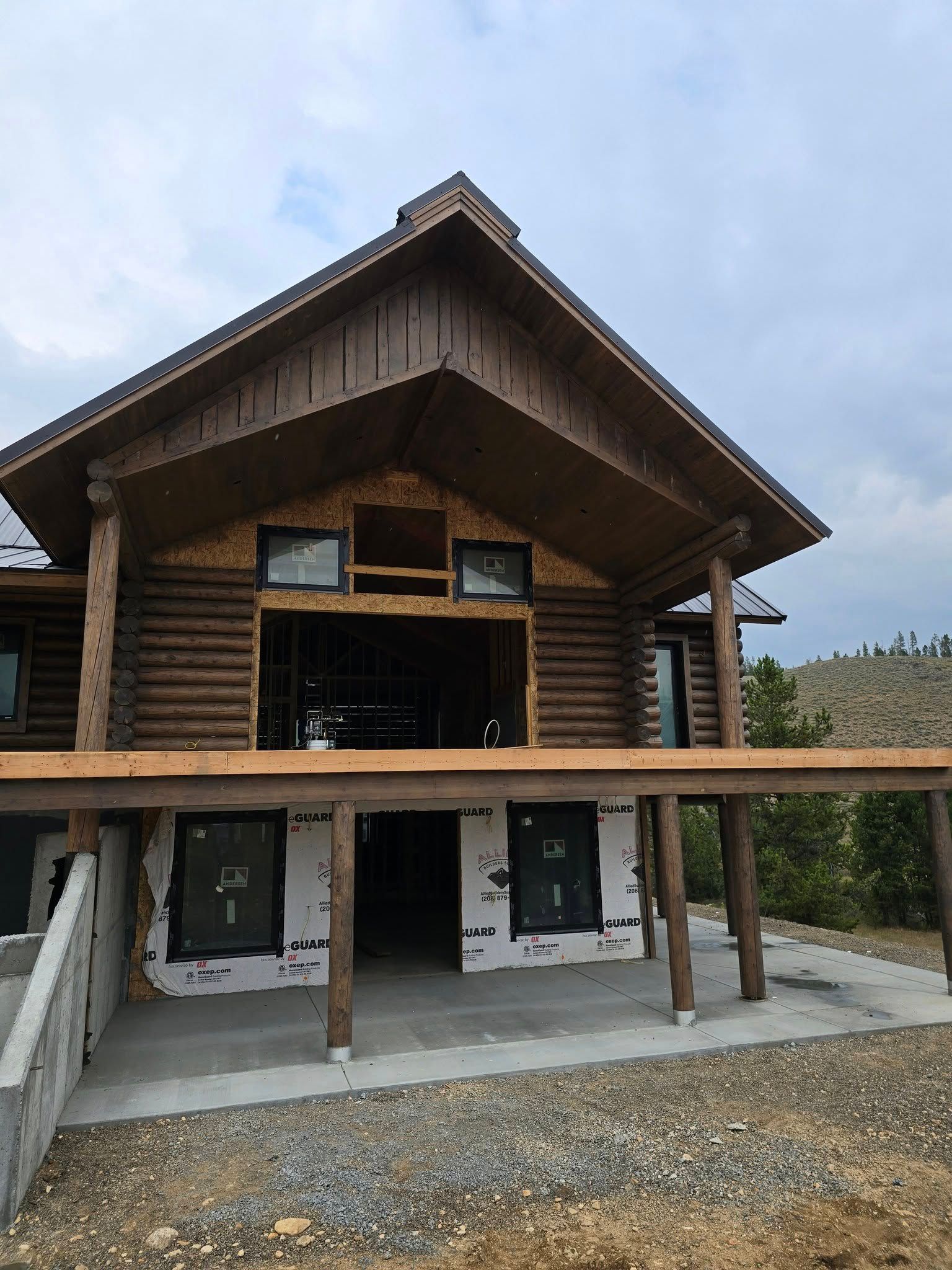 Log cabin under construction with a porch and concrete foundation.