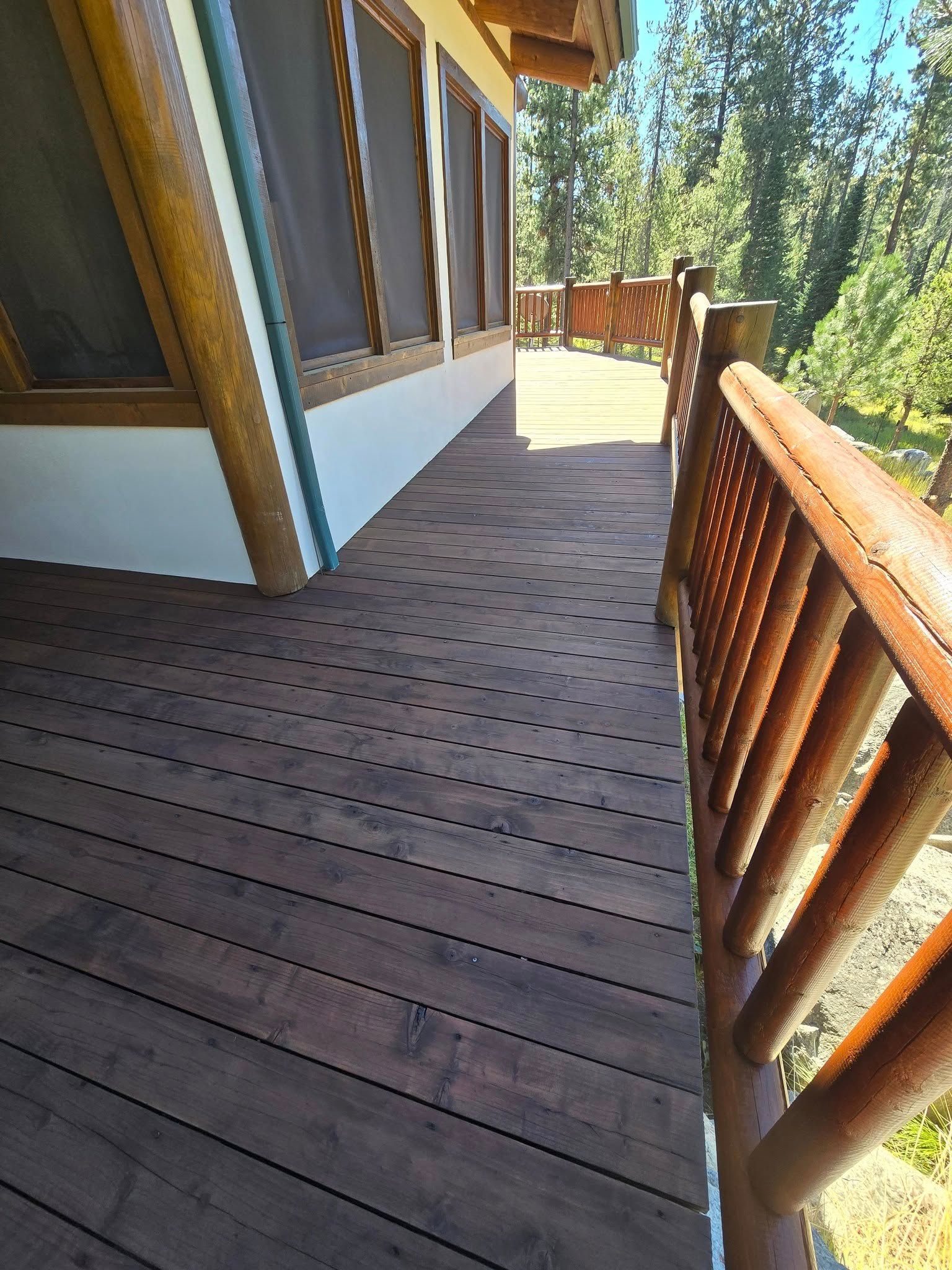 Wooden deck with log railing and siding, overlooking trees.