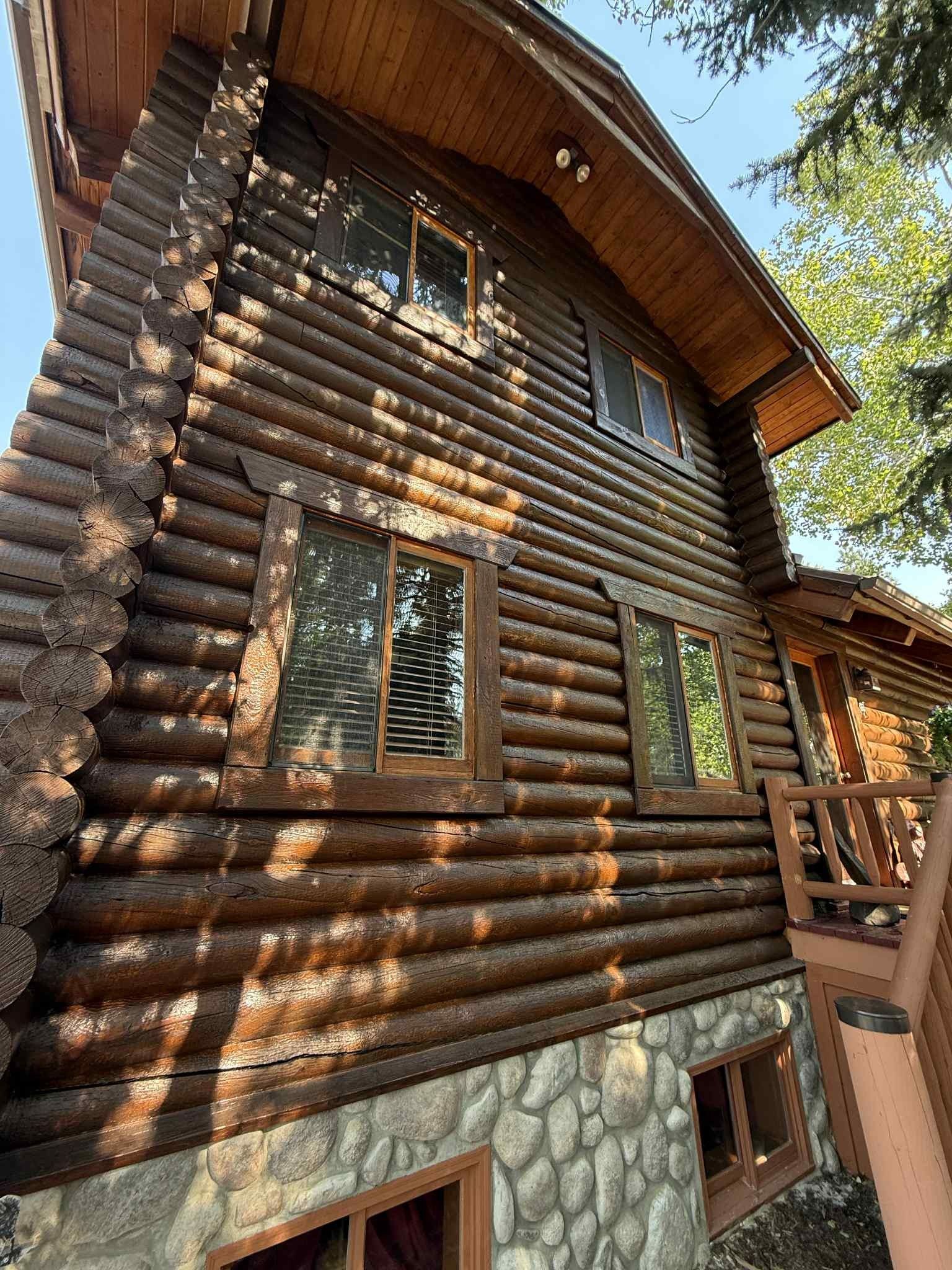 Log cabin with dark brown logs, stone foundation, and multiple windows.