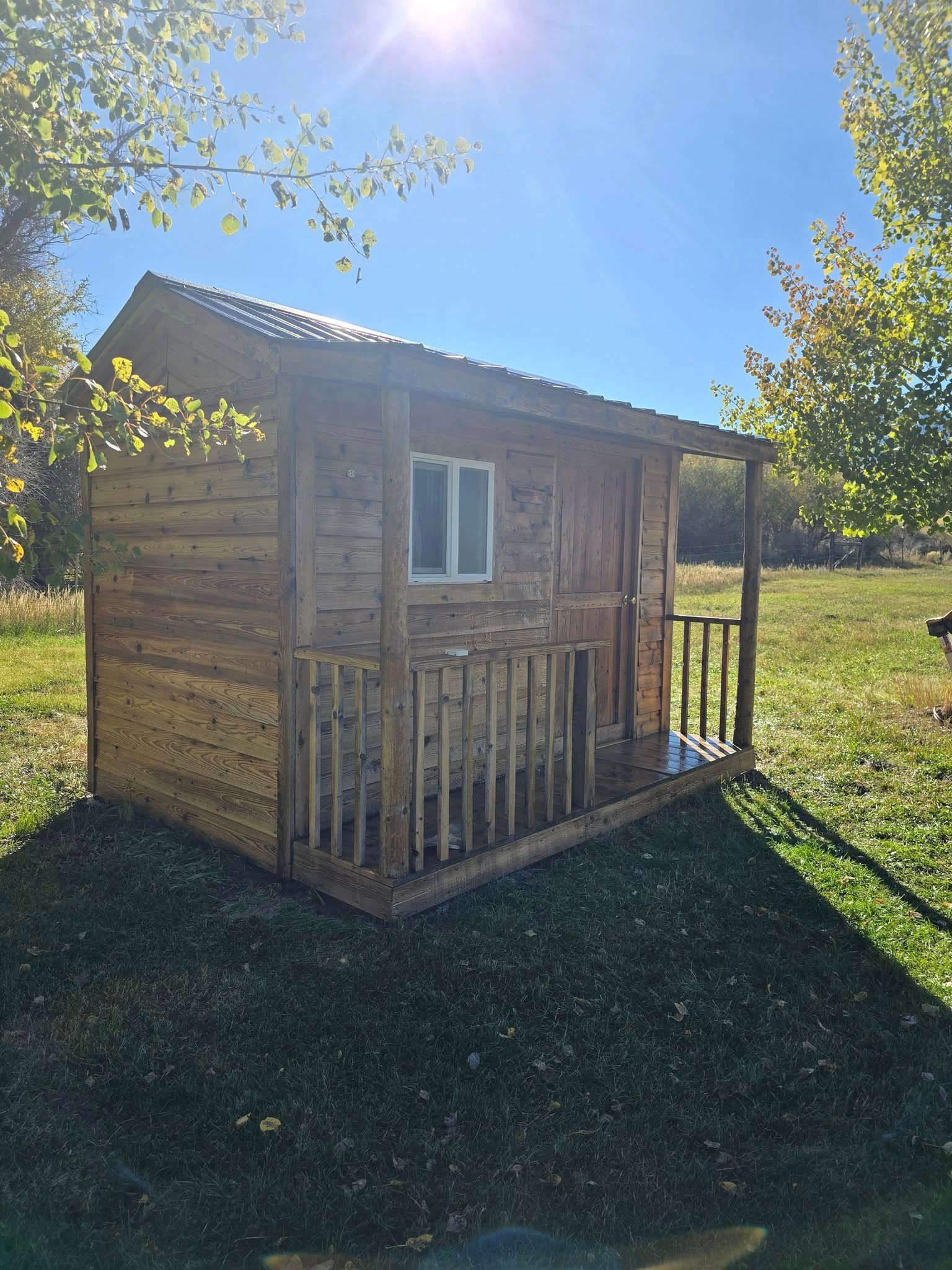 Wooden cabin with porch on a grassy lawn under a sunny sky.