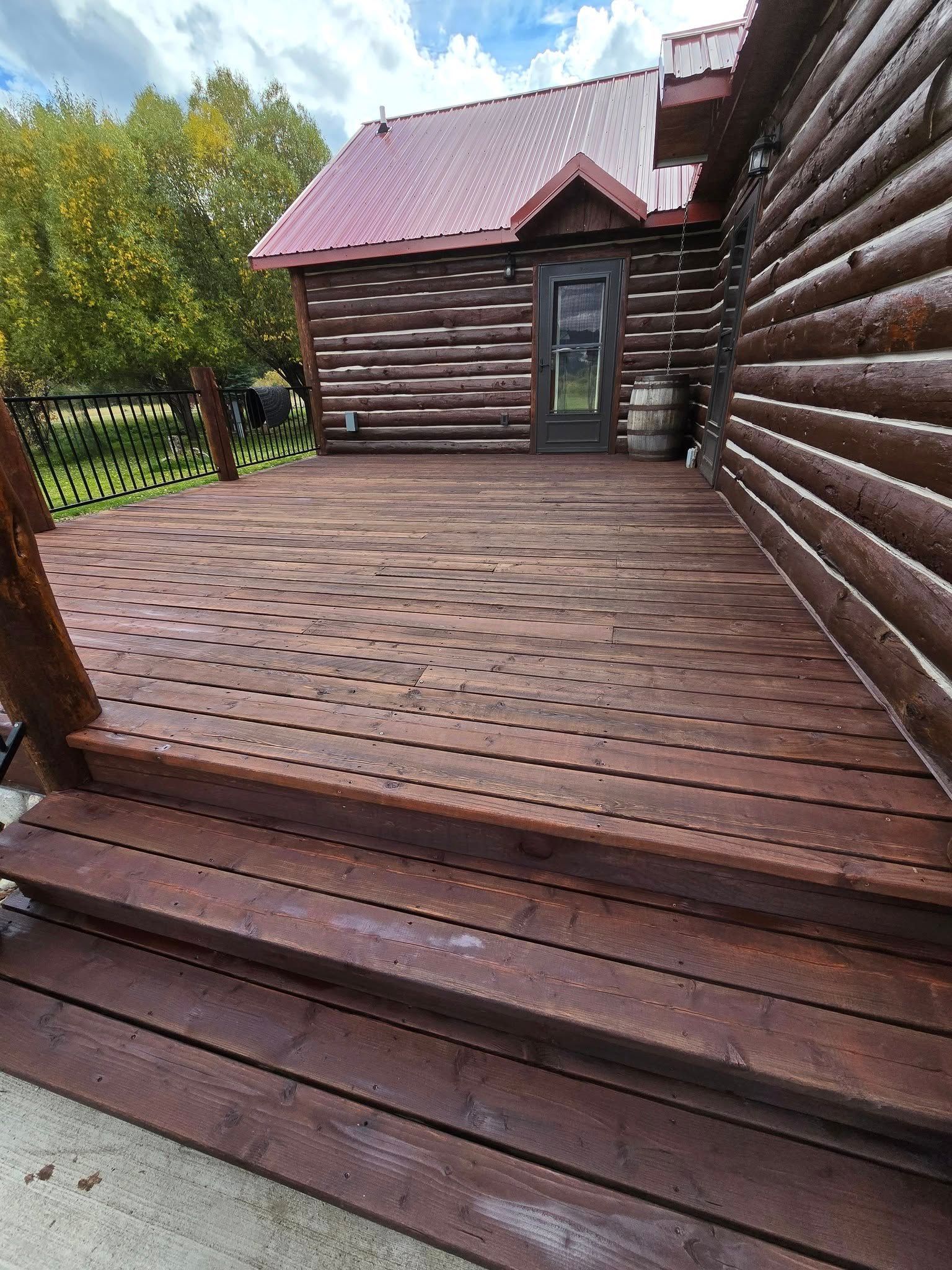 Wooden deck and stairs stained brown, next to a log cabin with red roof.