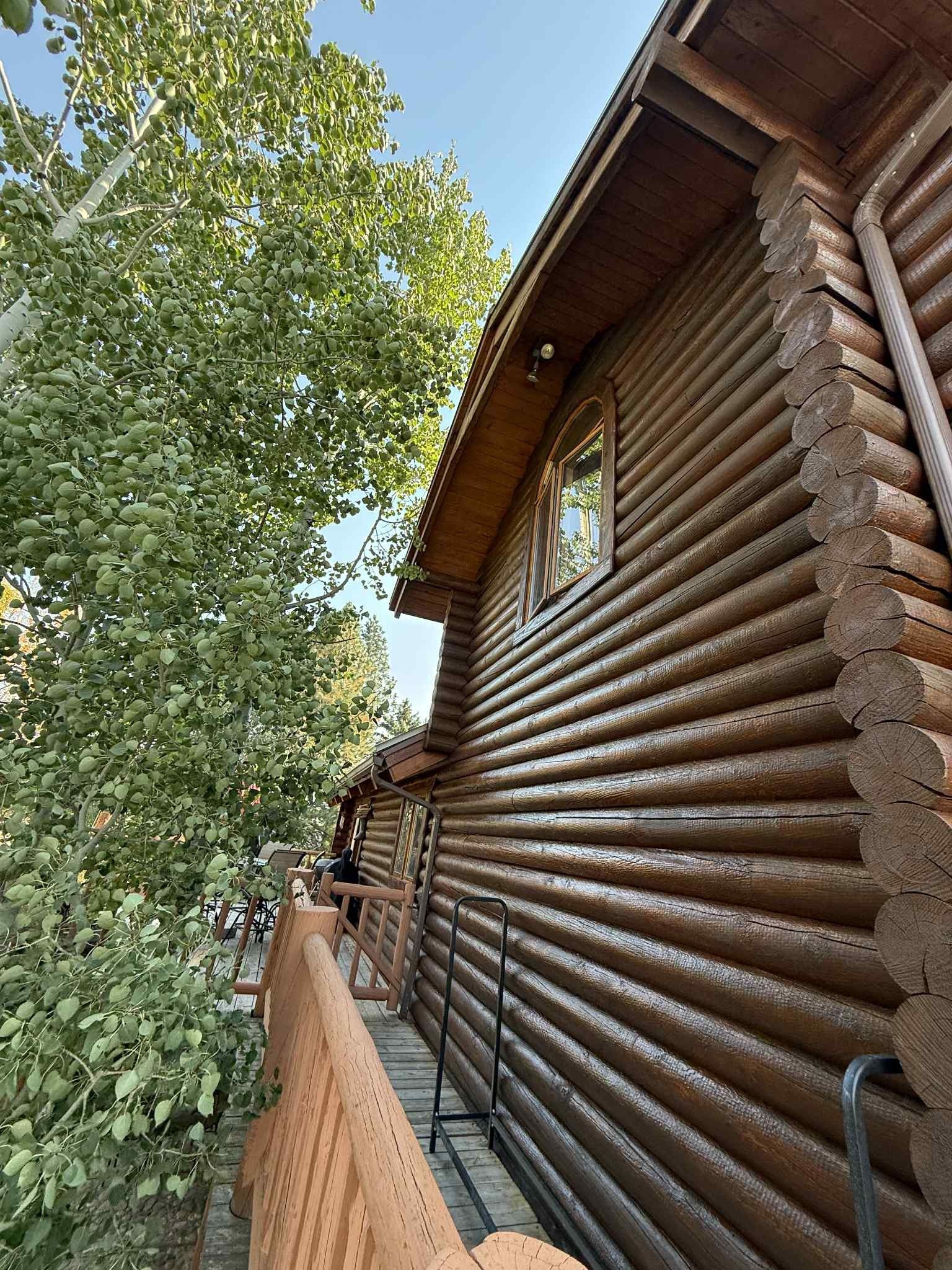 Wooden log cabin exterior with a balcony, trees, and blue sky.
