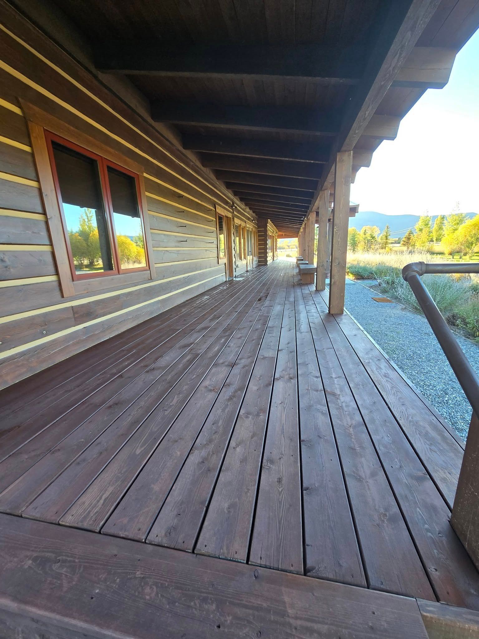 Wooden porch of a log cabin with a dark stain, overlooking a grassy field.