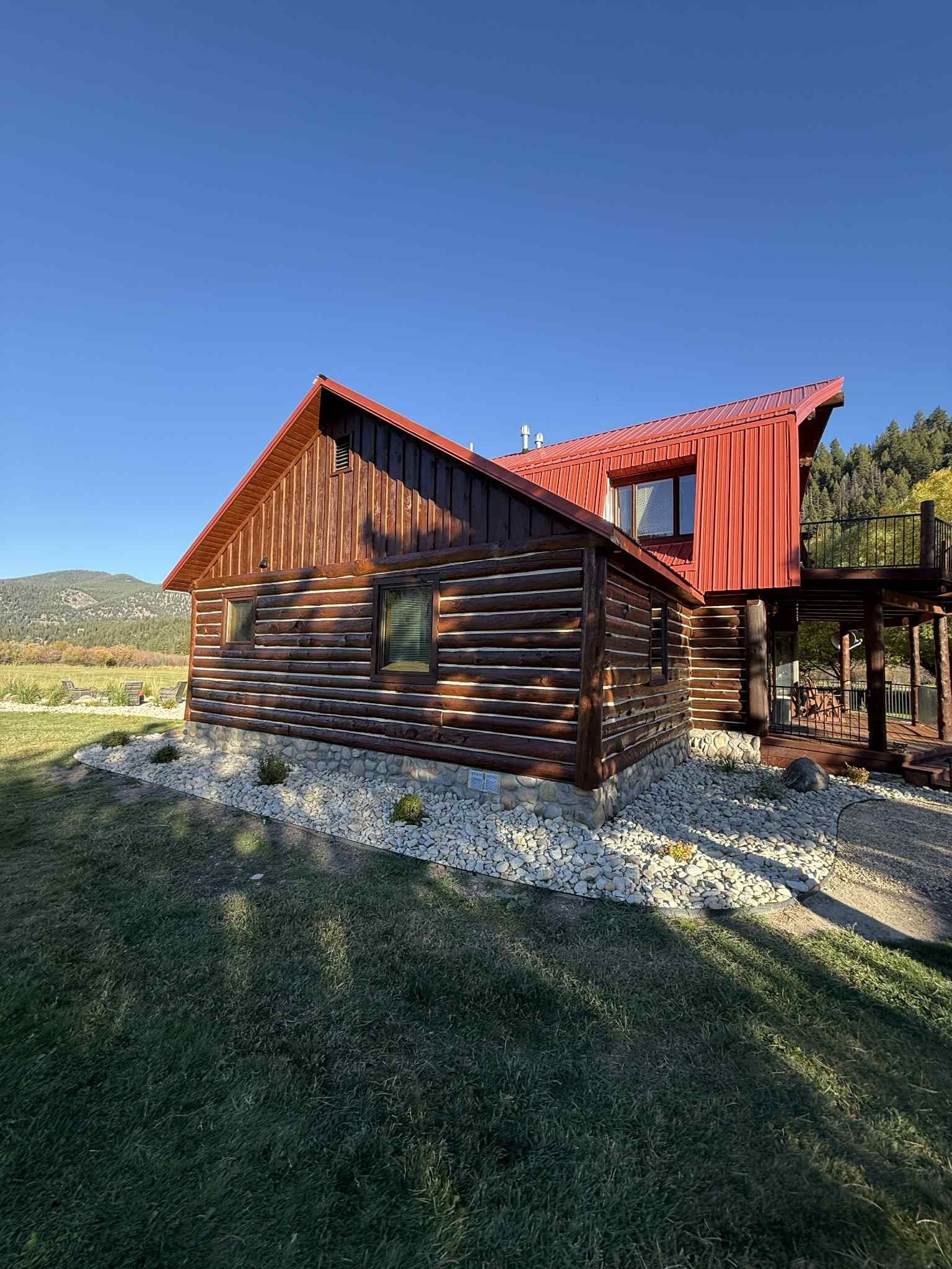 Log cabin with a red roof on a grassy hill; blue sky.