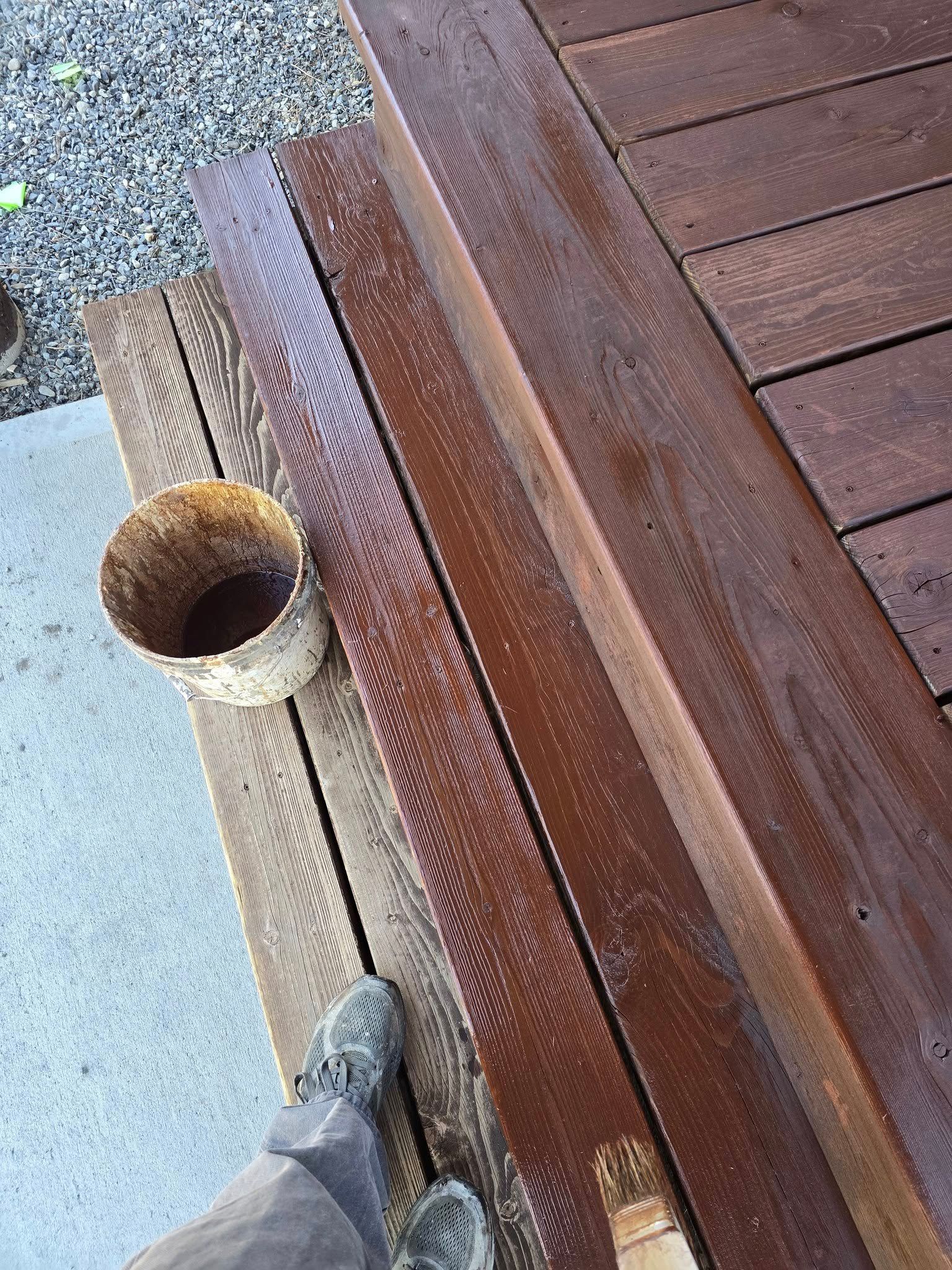 Applying brown stain to wooden boards with a brush, outside.