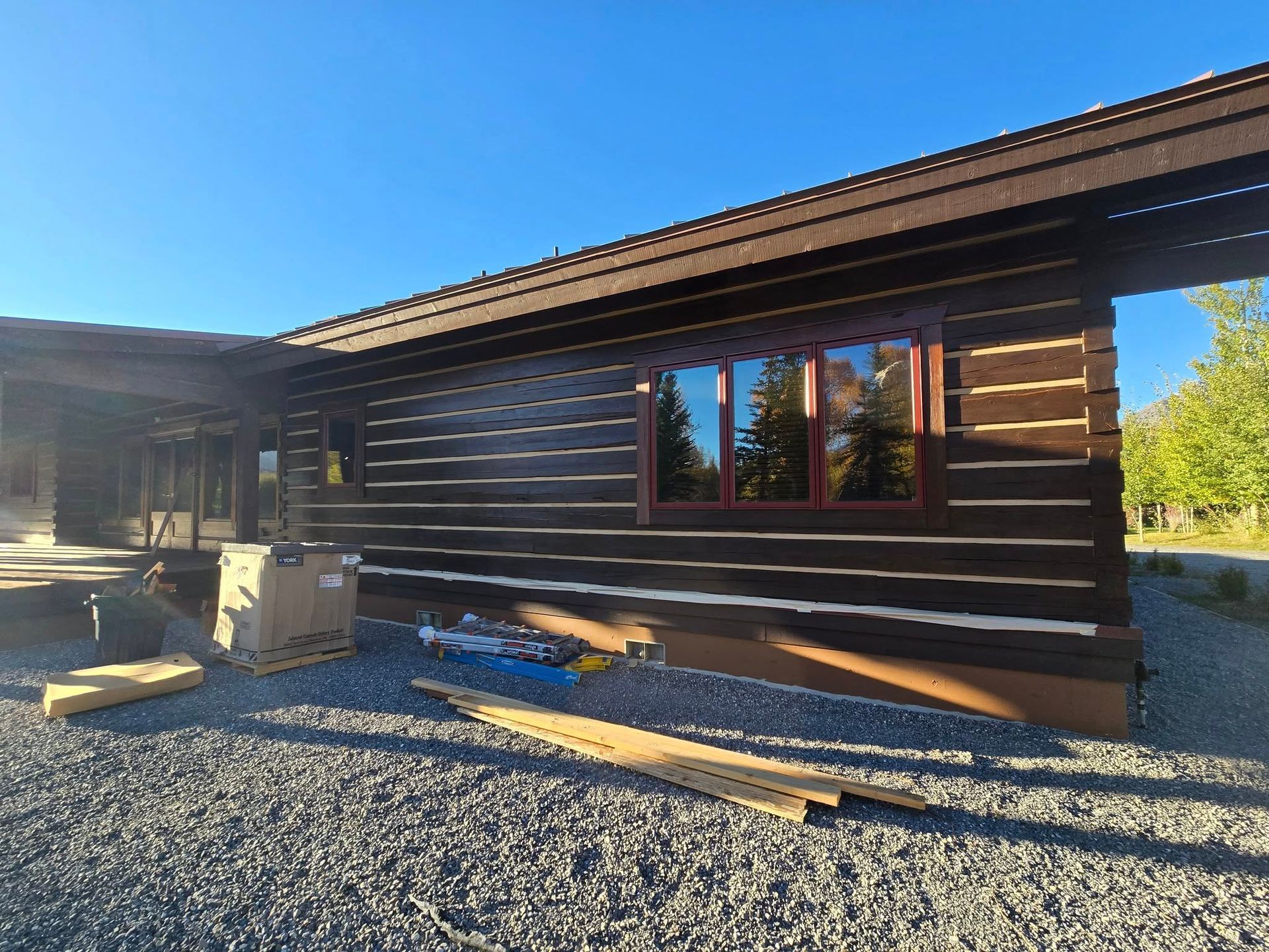 Exterior of a brown log cabin with a dark brown roof and a red-brown window frame under a blue sky.