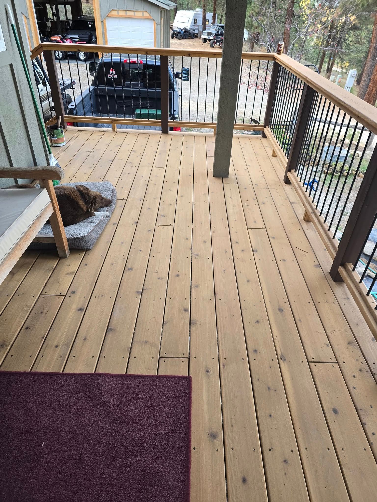 Wooden deck with railing, a purple rug, and a dog bed. A support column rises through the deck.
