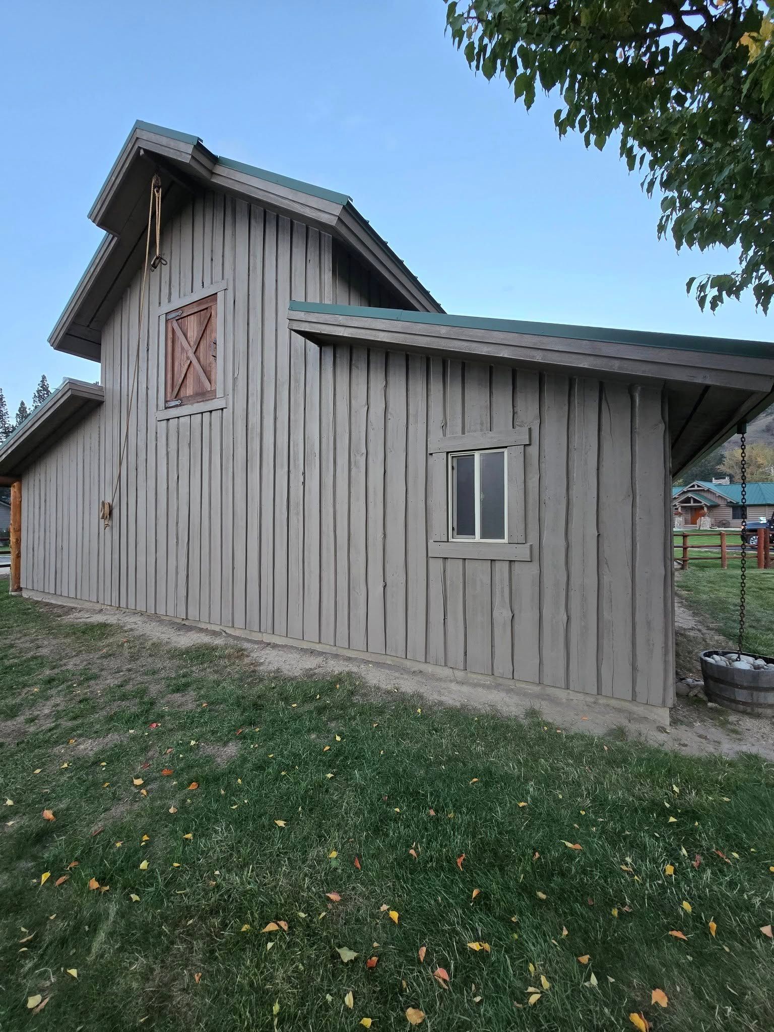 Light brown barn with green roof, grass and a small window.