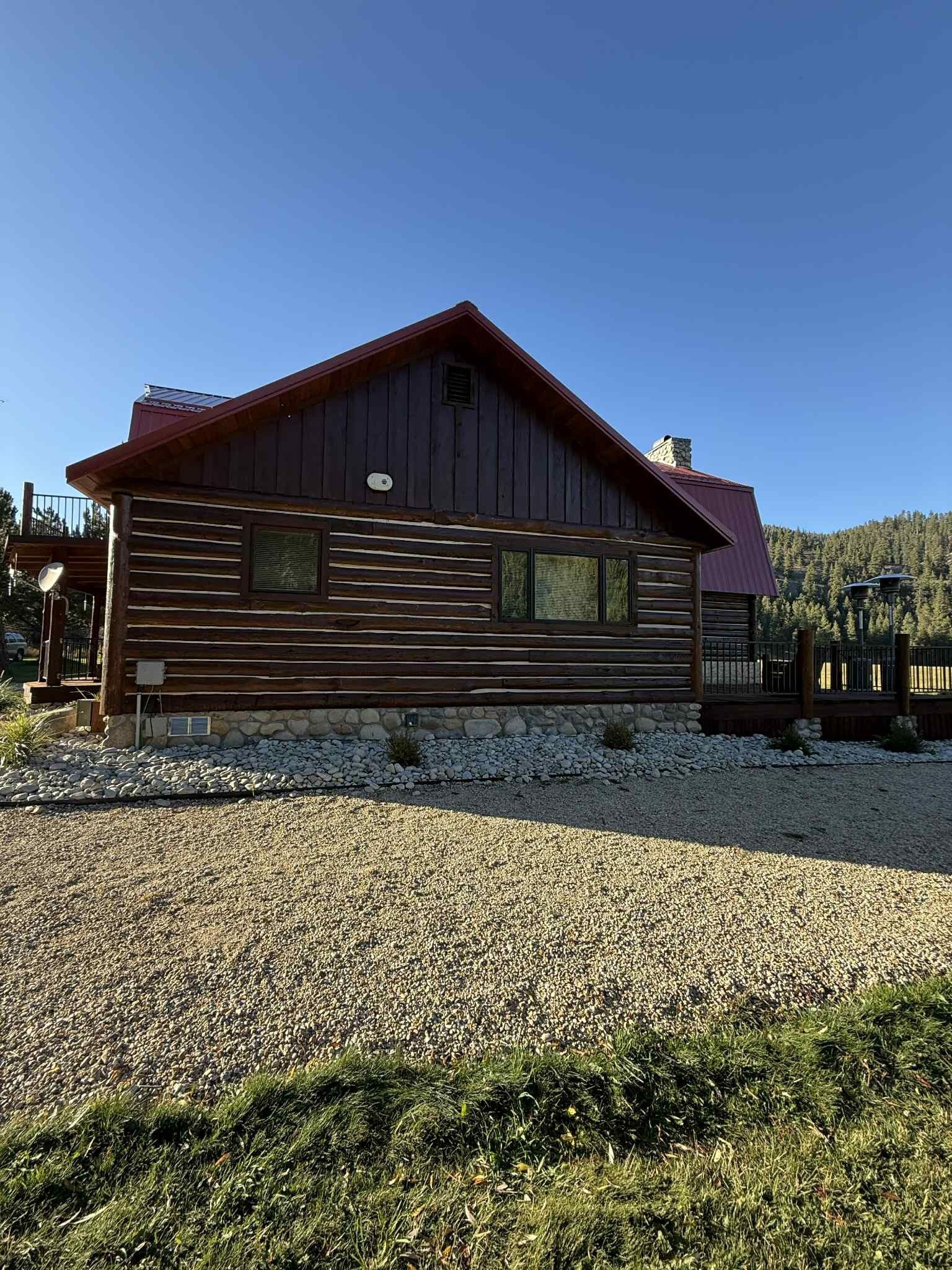 Log cabin with brown logs, red roof, and gravel yard.