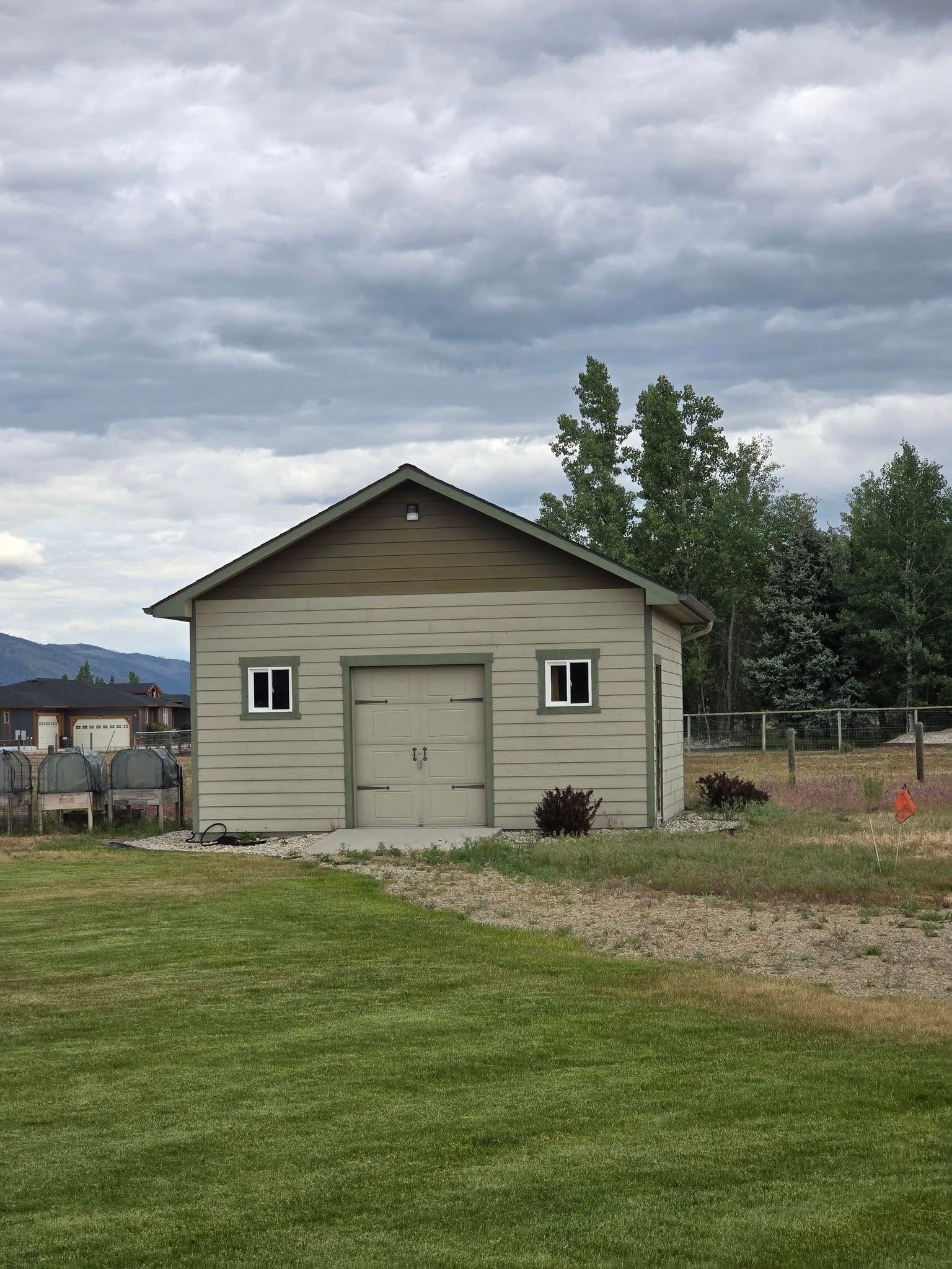 Tan garage with two windows, a closed garage door, and a brown roof against a cloudy sky.