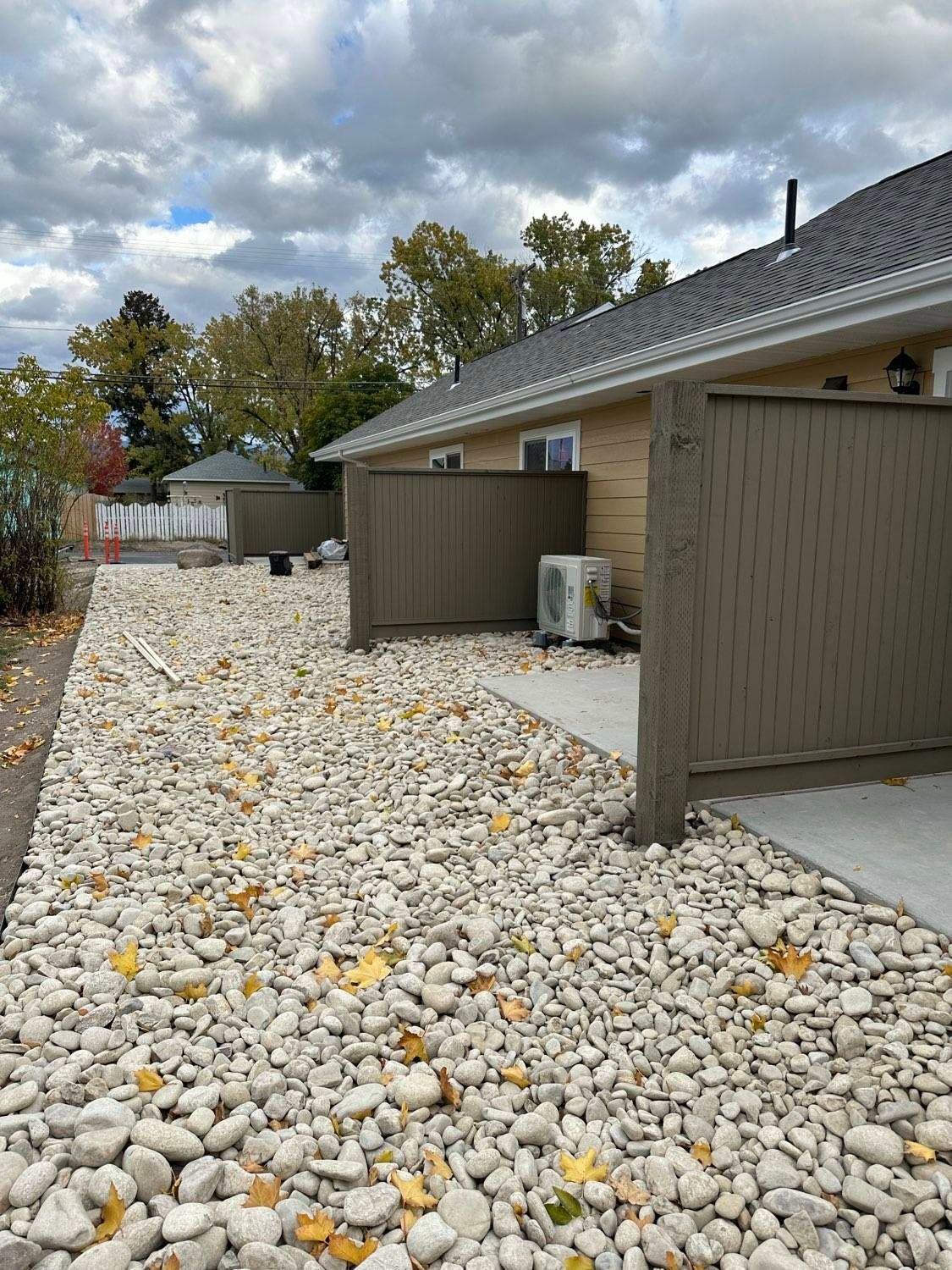Gravel pathway beside a tan building with a brown privacy fence, overcast sky.