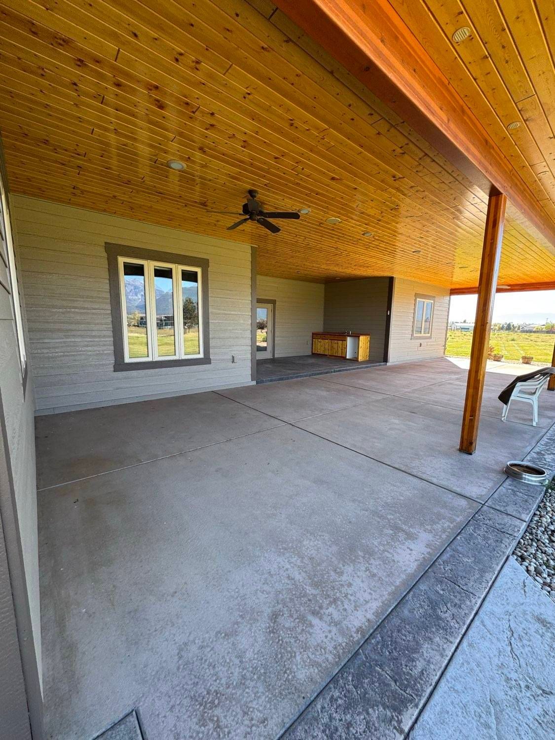 Covered patio with a concrete floor, wooden ceiling, and a ceiling fan.
