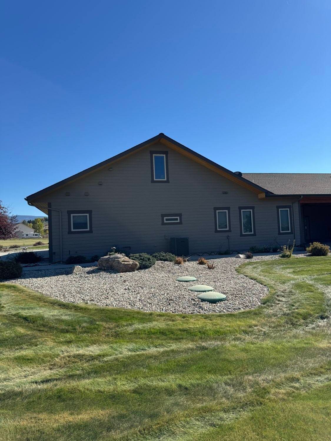 Side view of a gray house with a brown roof and a blue sky; landscaping in the yard.