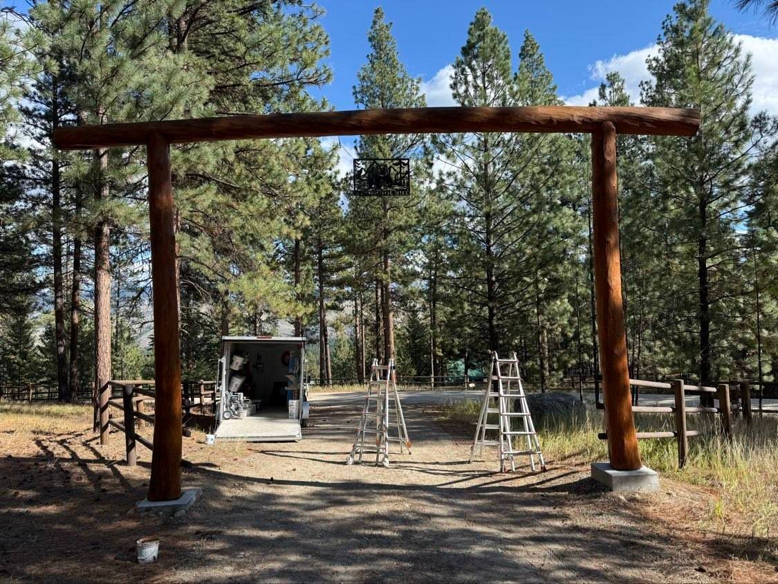 Wooden archway entrance with utility box, ladders, and forest backdrop.
