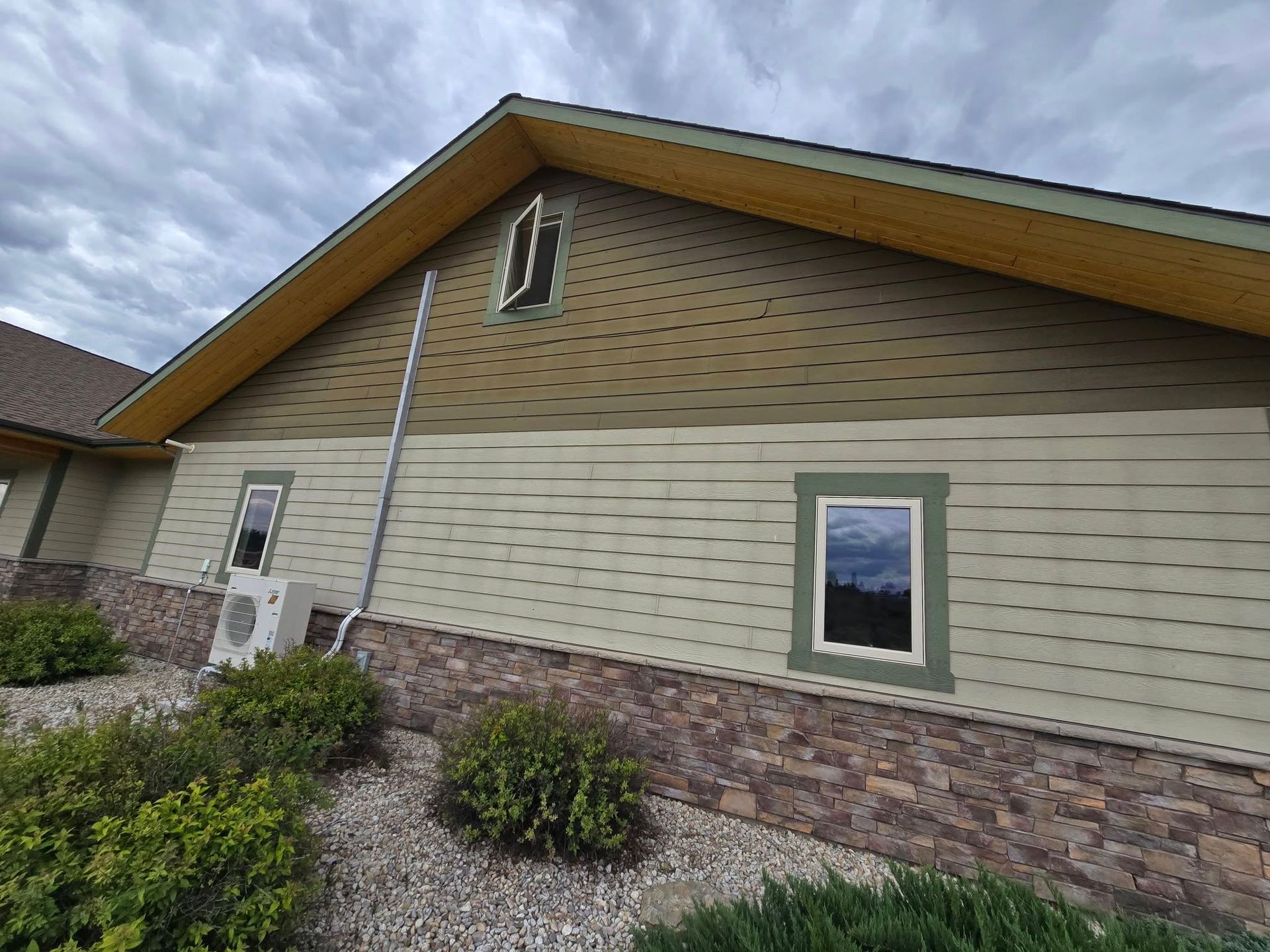 Exterior view of a house with green siding, brown stone base, and a cloudy sky.
