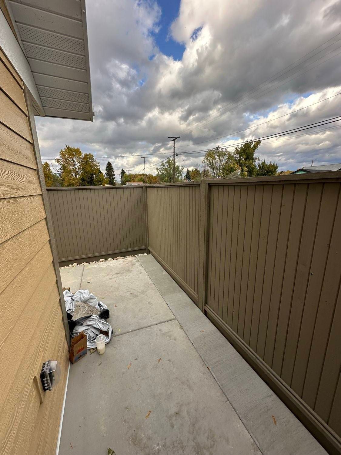 Enclosed concrete patio with tan fence and cloudy sky.  Siding on the left.